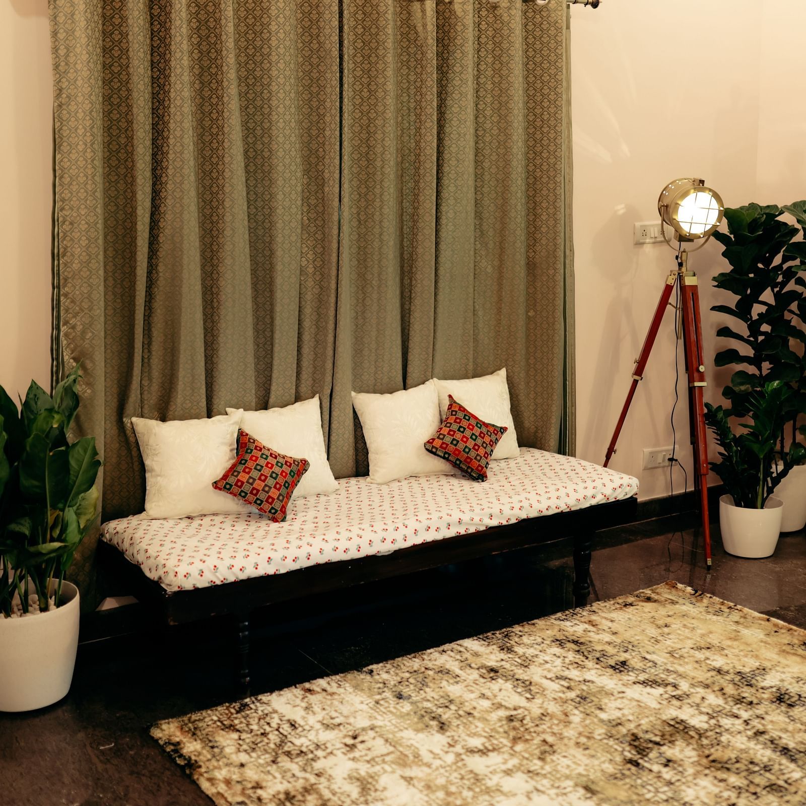 A small sofa with cushions, plants in pots, a standing lamp, and a rug in a room with curtains  | Adhyaya Heritage Reverbed