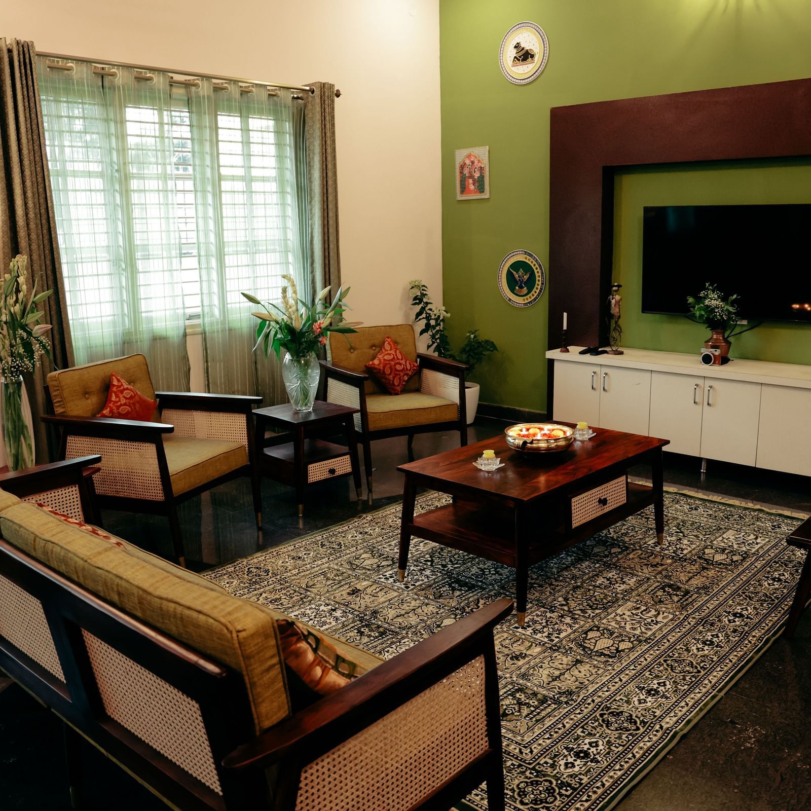 A living room with a green accent wall, a TV mounted on it, and a brown sofa set | Adhyaya Heritage Reverbed