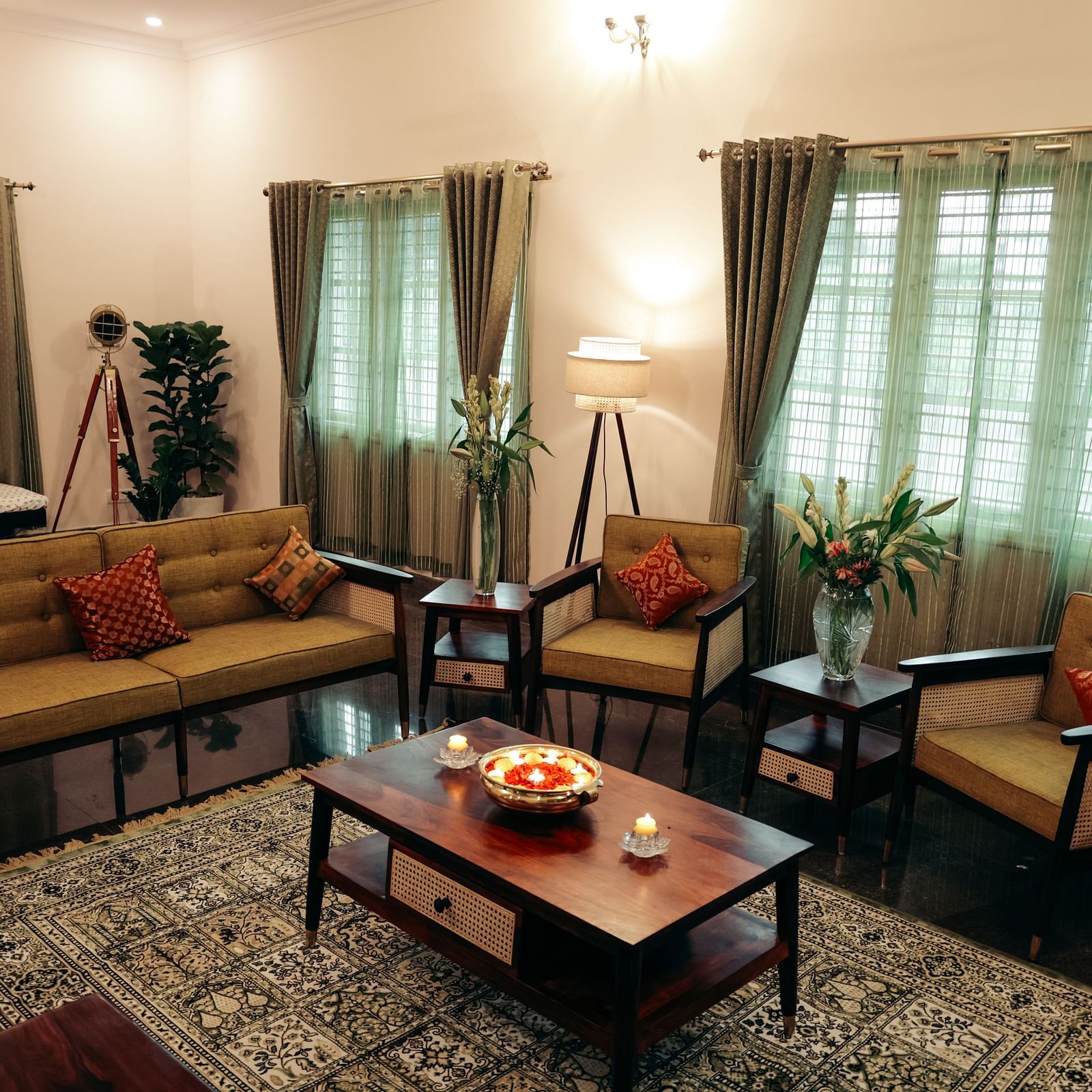 A living room with a brown sofa, two armchairs, a coffee table, and curtains on large windows | Adhyaya Heritage Reverbed