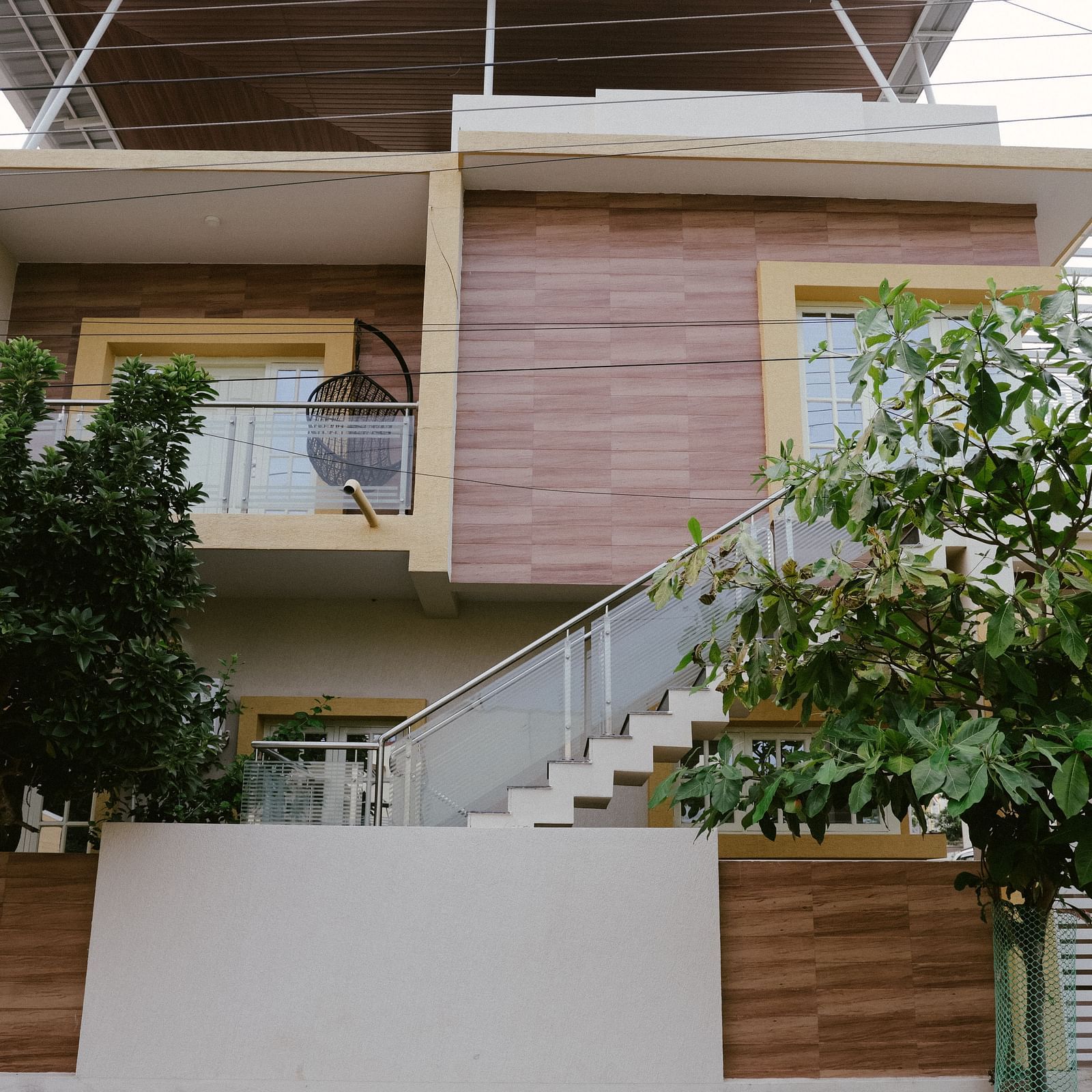 A modern two-story house with a combination of light-colored and wood-paneled exterior, featuring a staircase leading to an upper balcony.