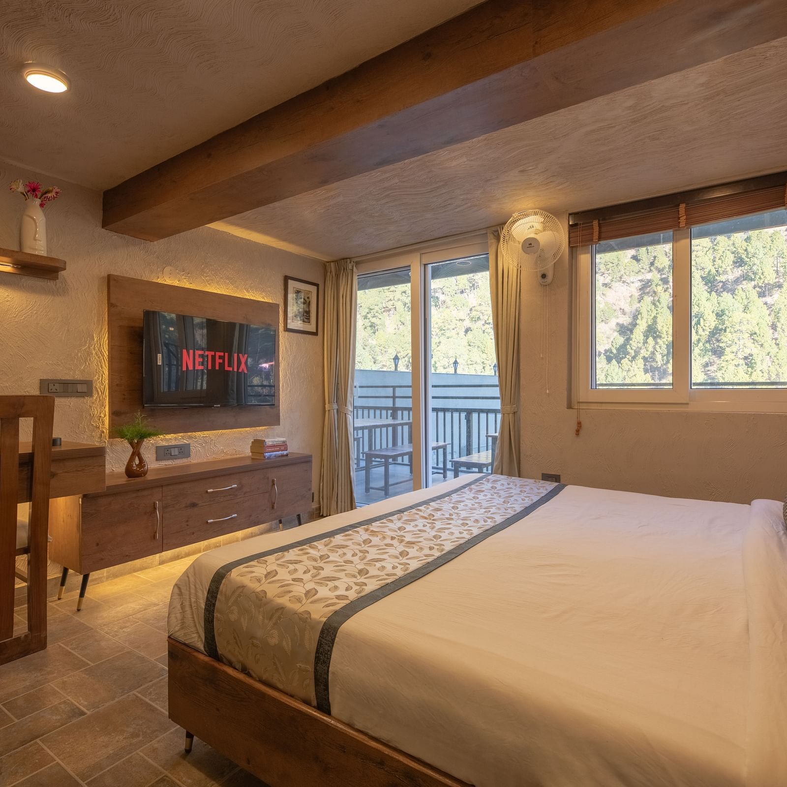 Room with double bed, TV, balcony doors, wooden beams on the ceiling, and soft lighting.