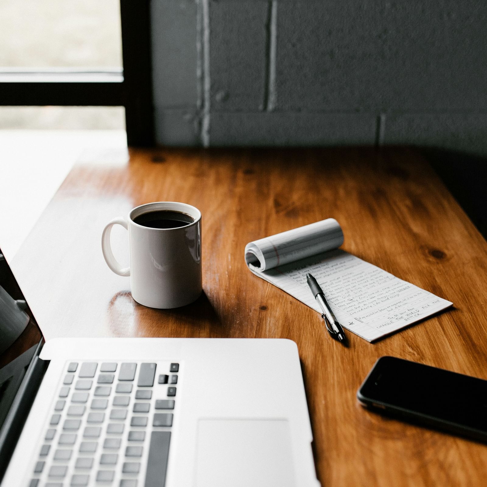 Laptop, coffee and notepad, phone on a table.