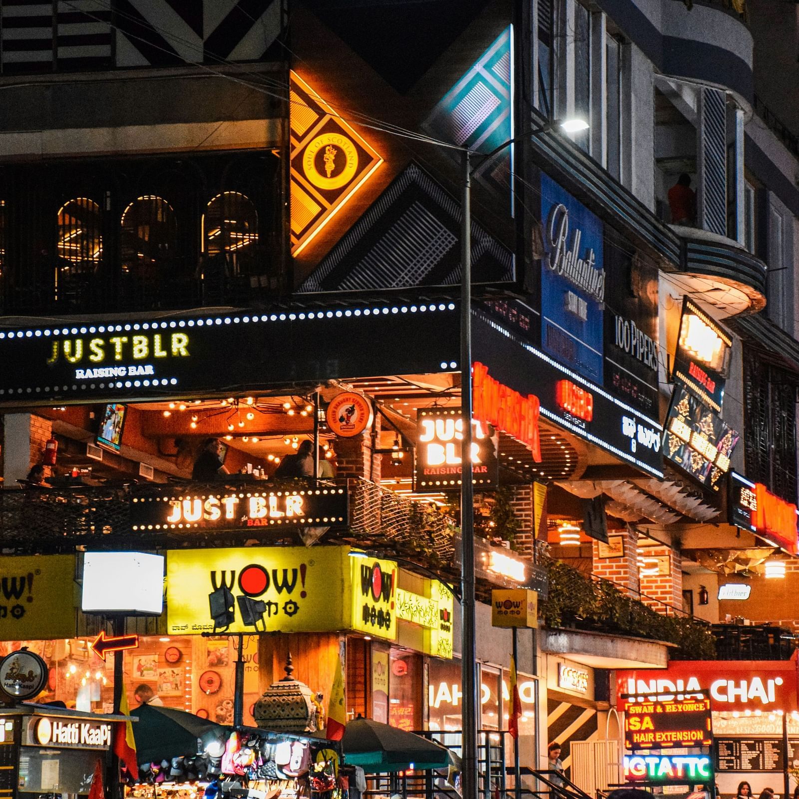 a bustling street with various dining outlets and shops during a late evening with brightly lit signboards