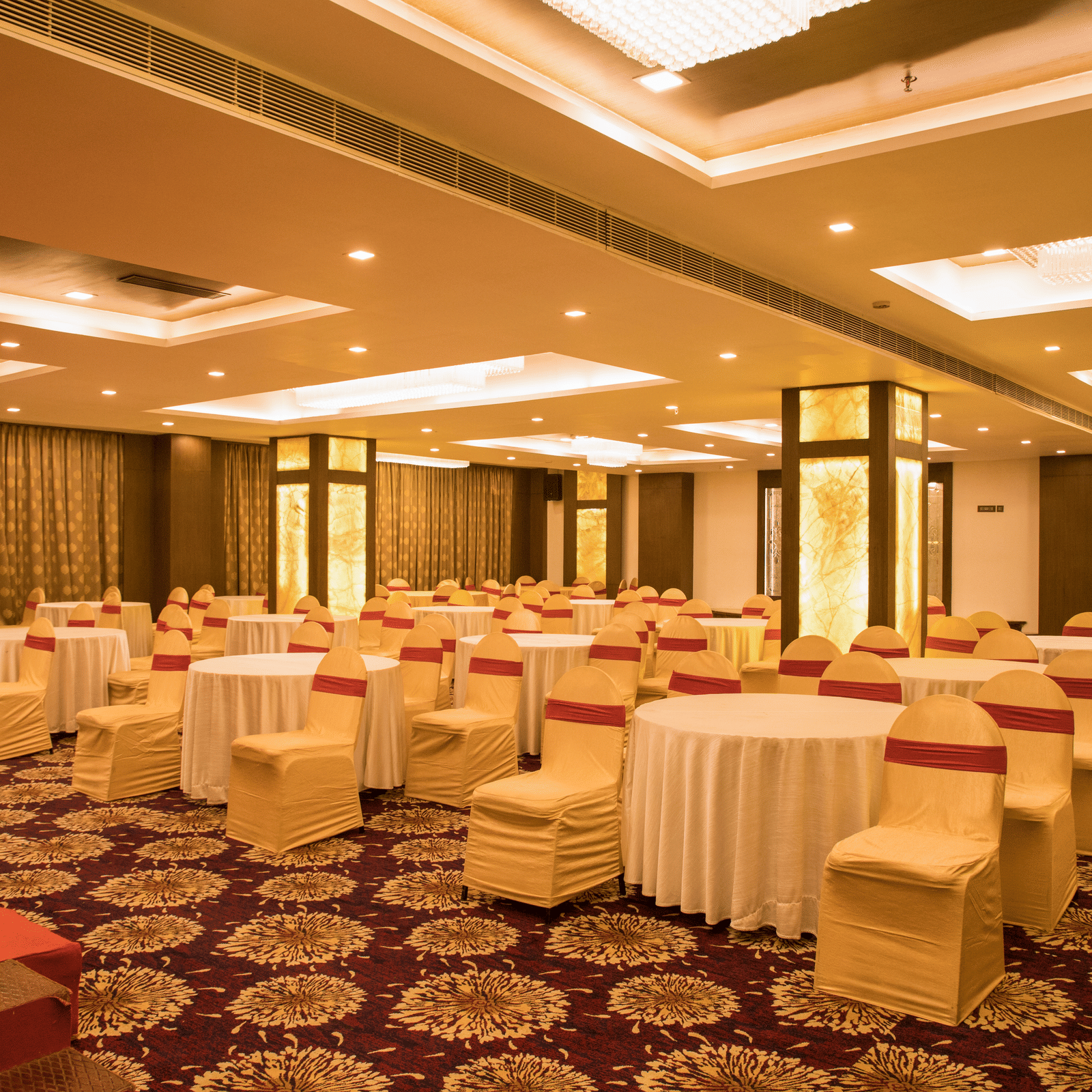 A spacious banquet hall at Benzz Park Chennai with numerous round tables draped in white, set for a gathering.