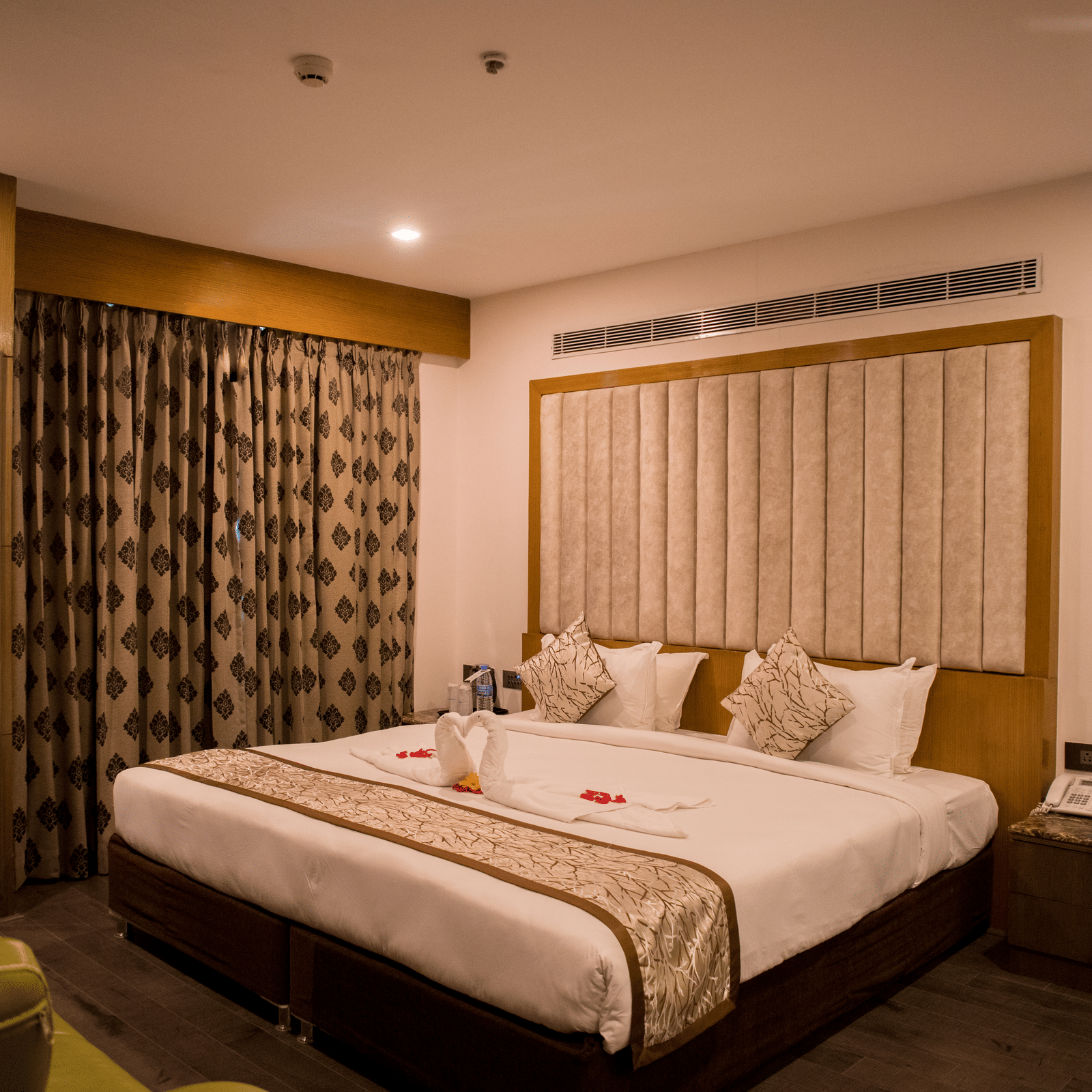 A hotel room at Benzz Park Chennai featuring a neatly made bed with white linens, a bedside table, and curtains.