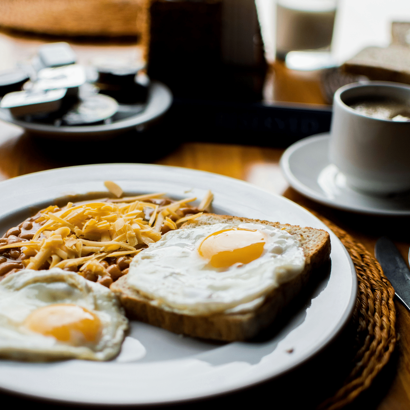  A plate of breakfast food with noodles and fried eggs, a cup of coffee, and cutlery on a table.