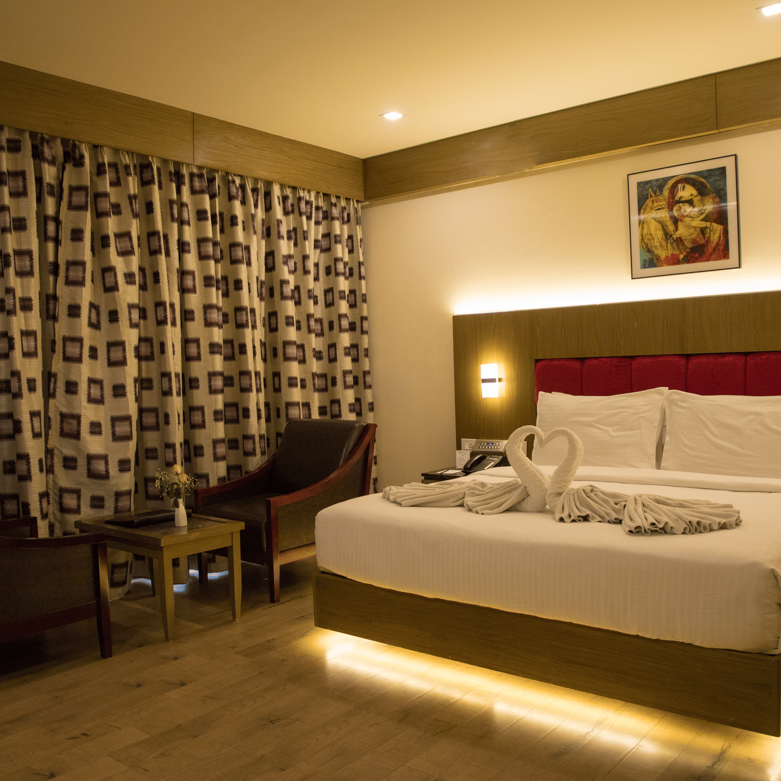 Full view of the Deluxe Room at the Benzz Park, Vellore, featuring a double bed with under-bed lights alongside a common seating area.