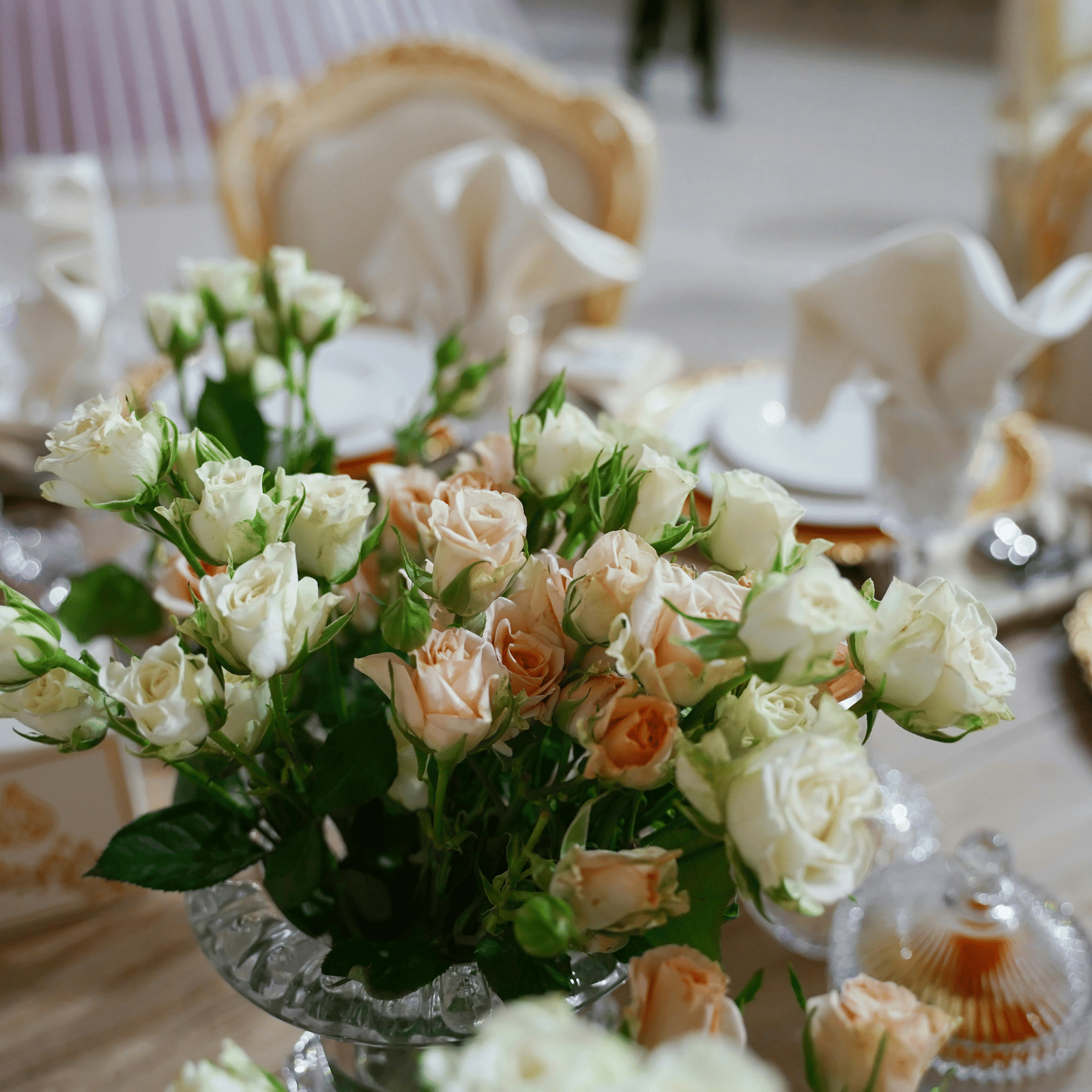 A close up shot of a beautiful flower vase with a lot of white and pink roses on a dining table.