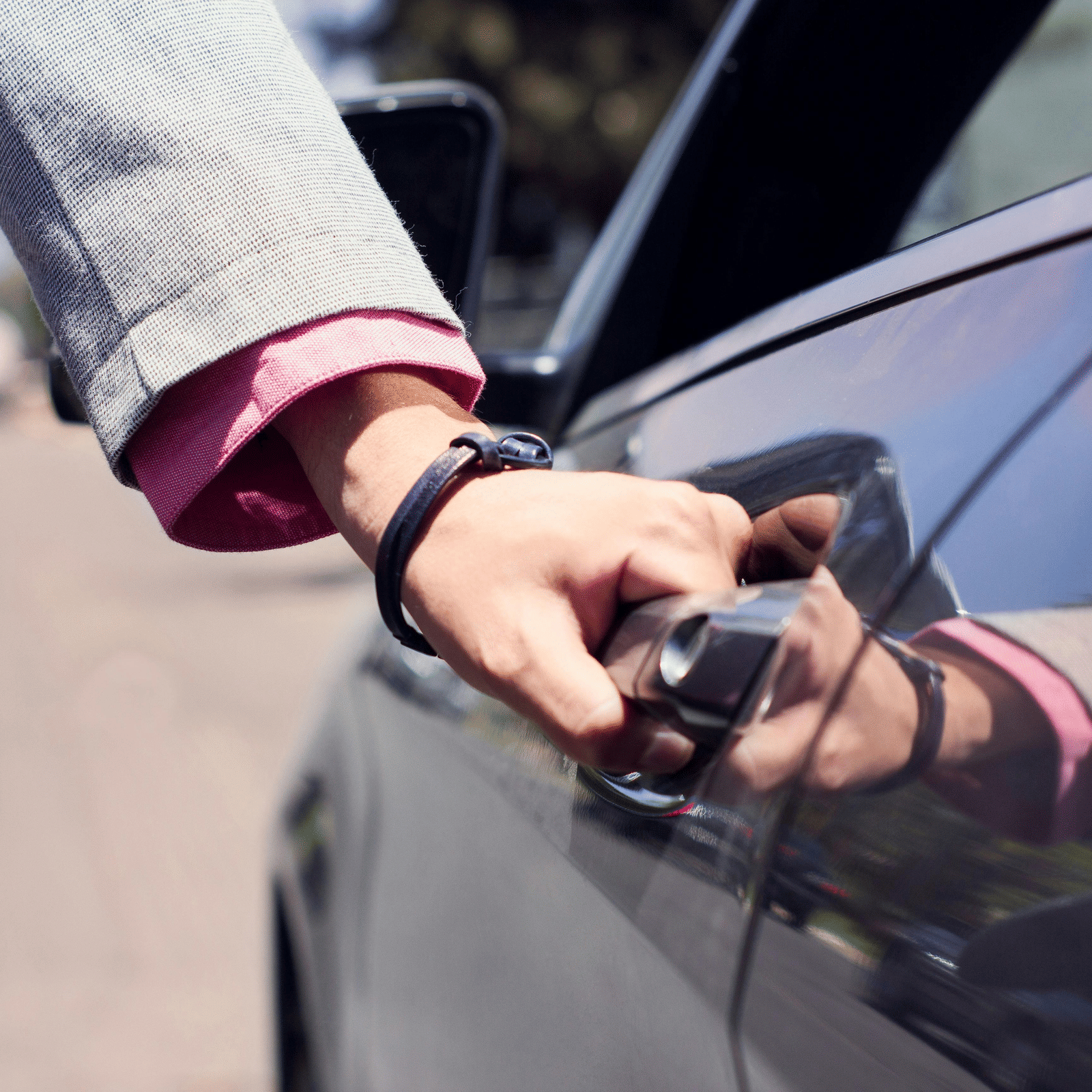 A person dressed in business formals opening the door of a car.
