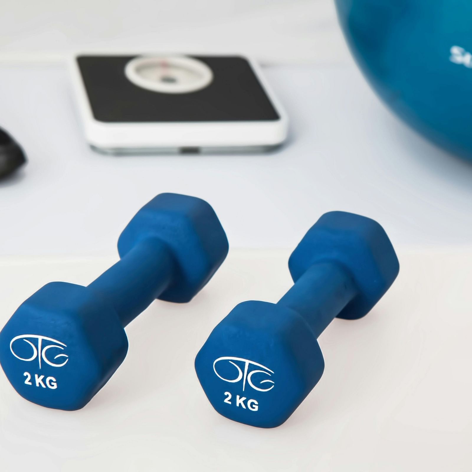 Two blue dumbbells, a smartphone, and athletic shoes on a light surface.