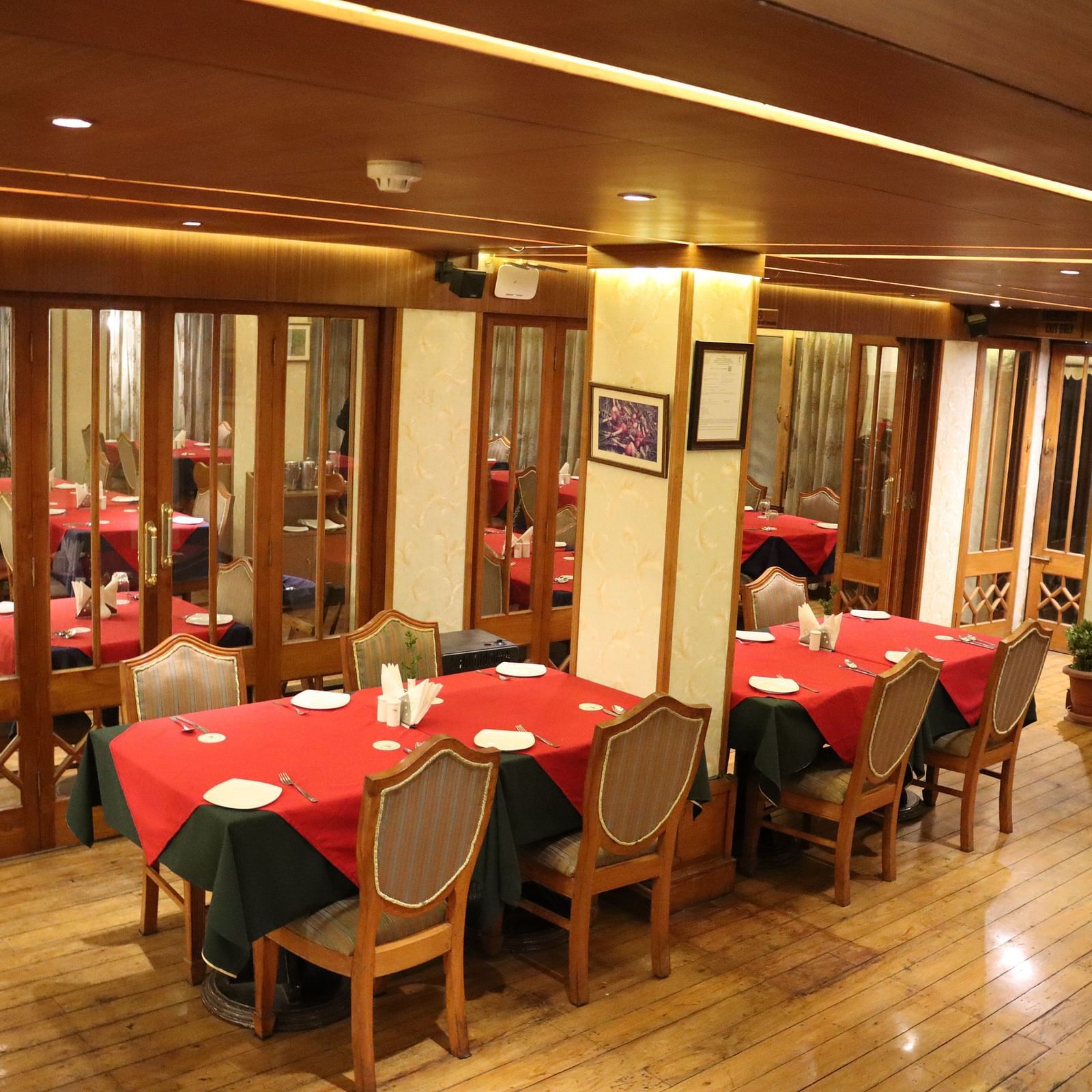 Dining area at Cedar Inn, Darjeeling, featuring spacious seating arrangements, neatly placed cutlery, overhead lighting and a CCTV.