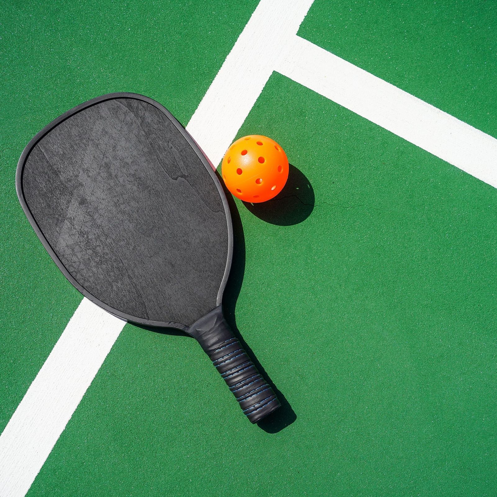 Image of a pickle ball and its racket kept on a green coloured court