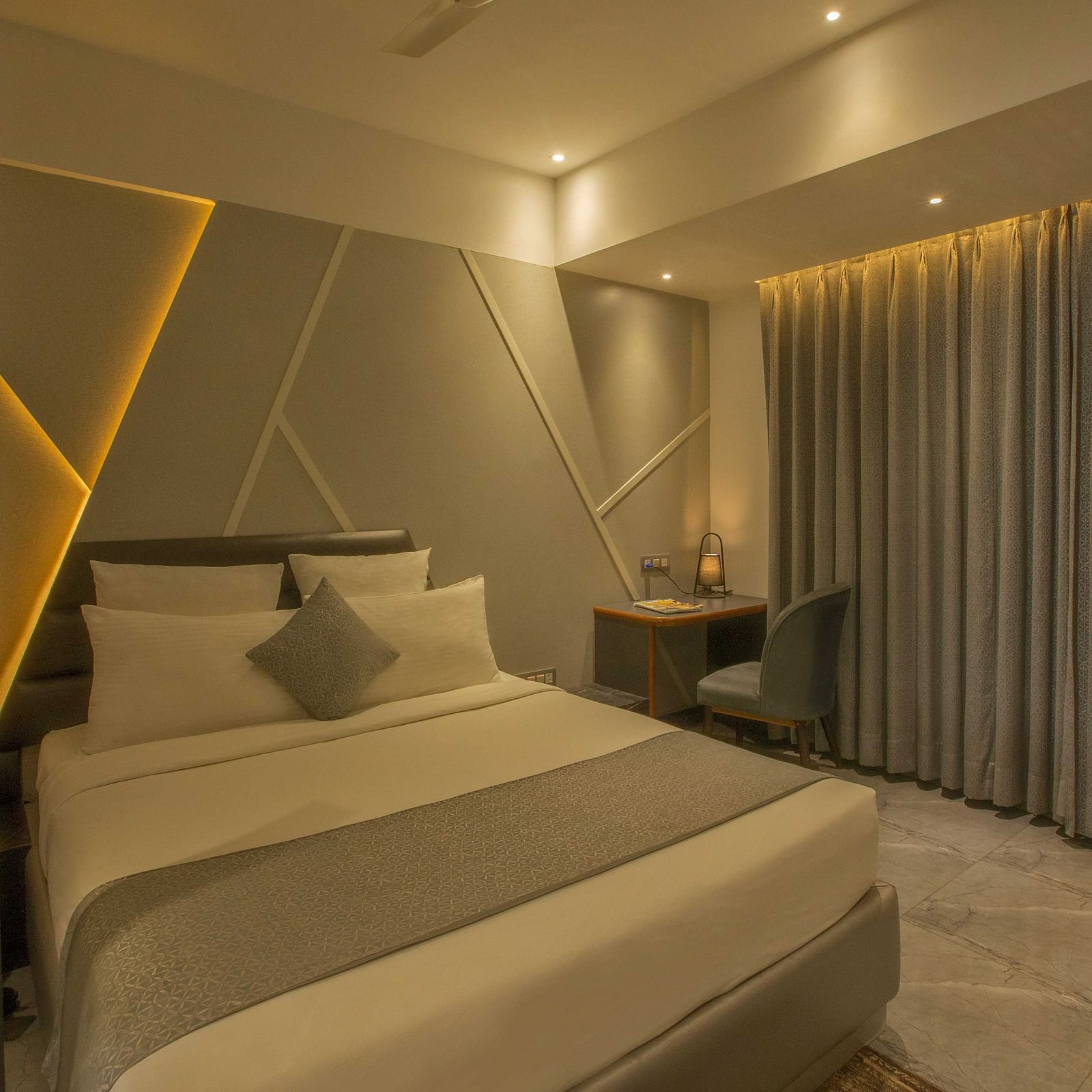 Image of well lit Coral Premium Room at Coral Reef Hotel and Spa in Port Blair featuring a plush bed and a work desk and chair next to it near the window