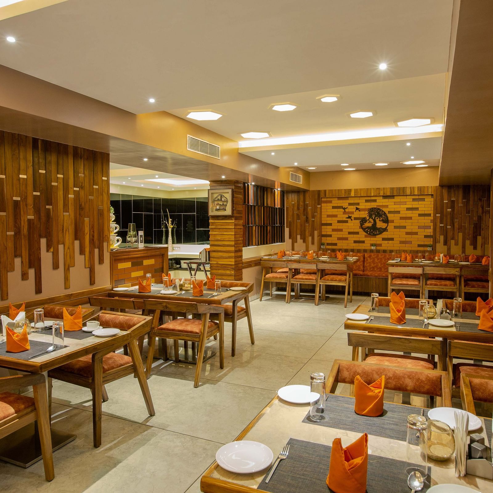 Image of Honeycomb Restaurant at Coral Reef Hotel & Spa in Port Blair showing dining setting of 4 chairs at each table and cutlery organised