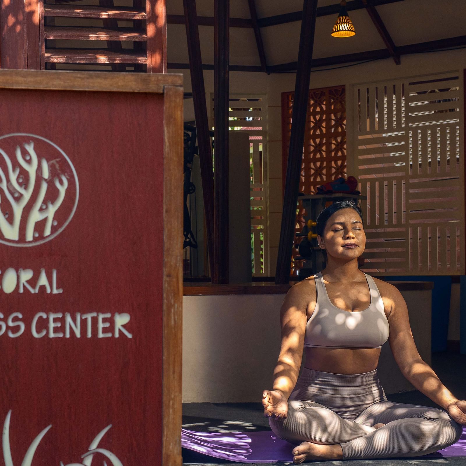 : A sign for the  Opal Fitness Center displayed alongside a statue of a person in a meditative pose. The background includes rustic wooden elements and a calm environment - Coral Reef Resort & Spa, Havelock
