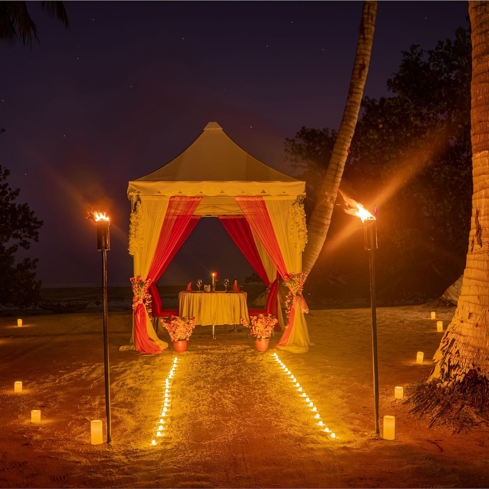 A canopy set up on a beach at night with a path of candles leading to it and torches on either side - Coral Reef Resort & Spa, Havelock