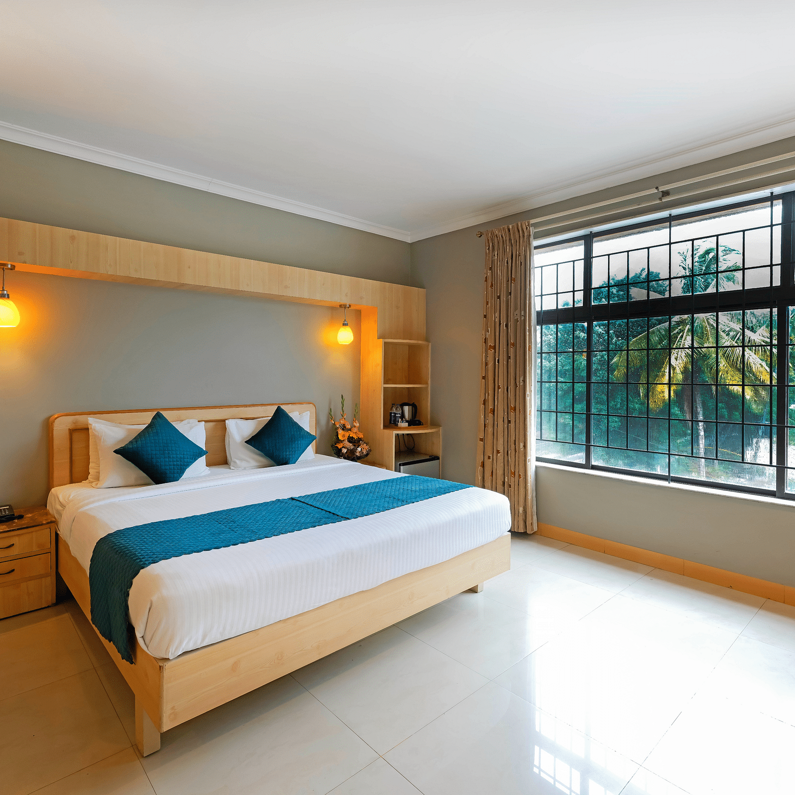 An image of a hotel room in Bengaluru featuring a queen size bed, a night stand, and sunlight from the expansive windows - Cross Roads Inn, Bengaluru