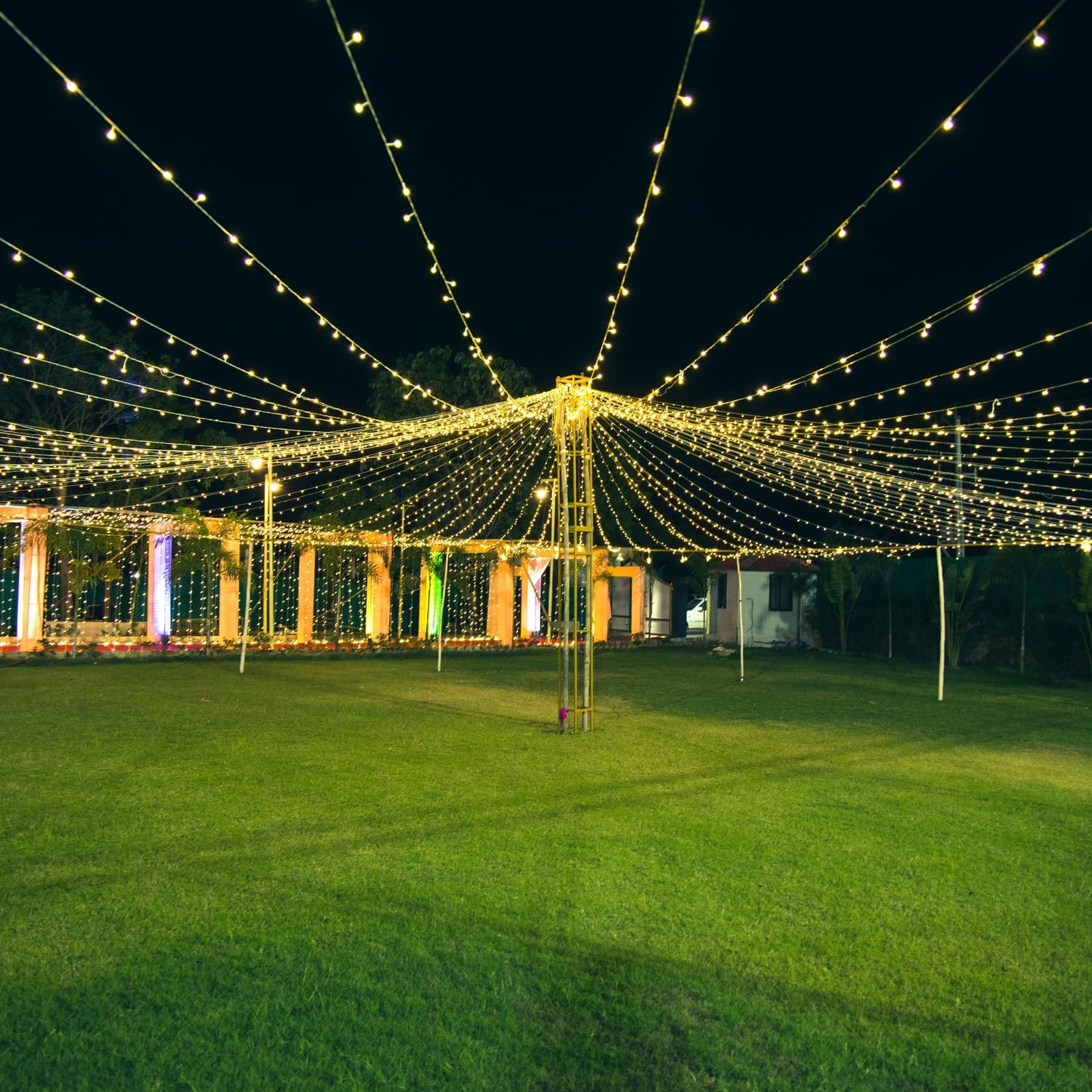 A wide view of lush lawn illuminated with hanging fairy lights arranged for an event at Daksh Resort and Amusement Park.