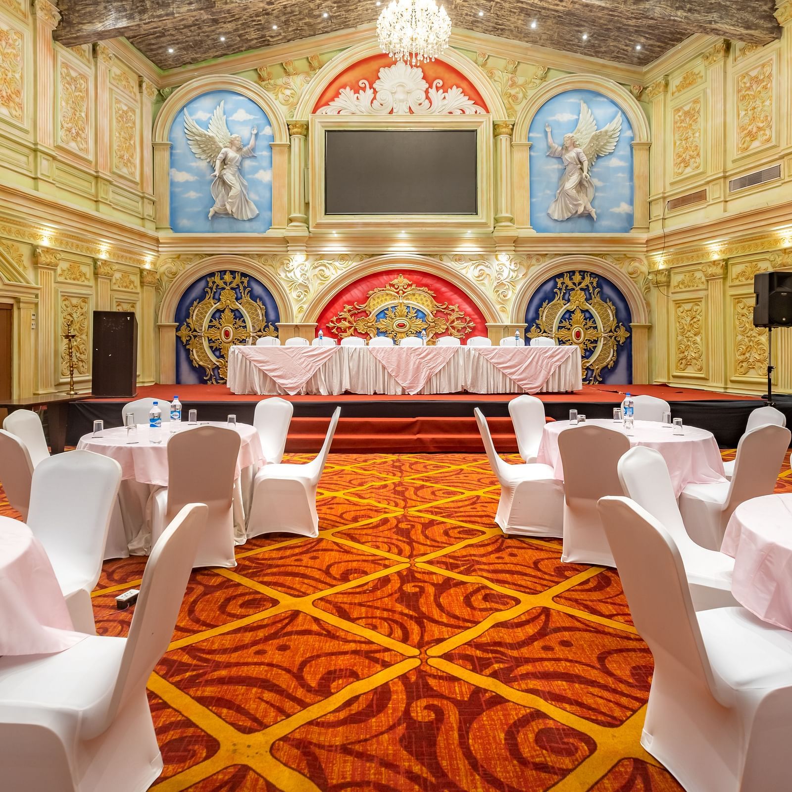 Elegantly decorated banquet hall at Diamond Palace Lords Plaza set with round tables and chairs facing a stage.