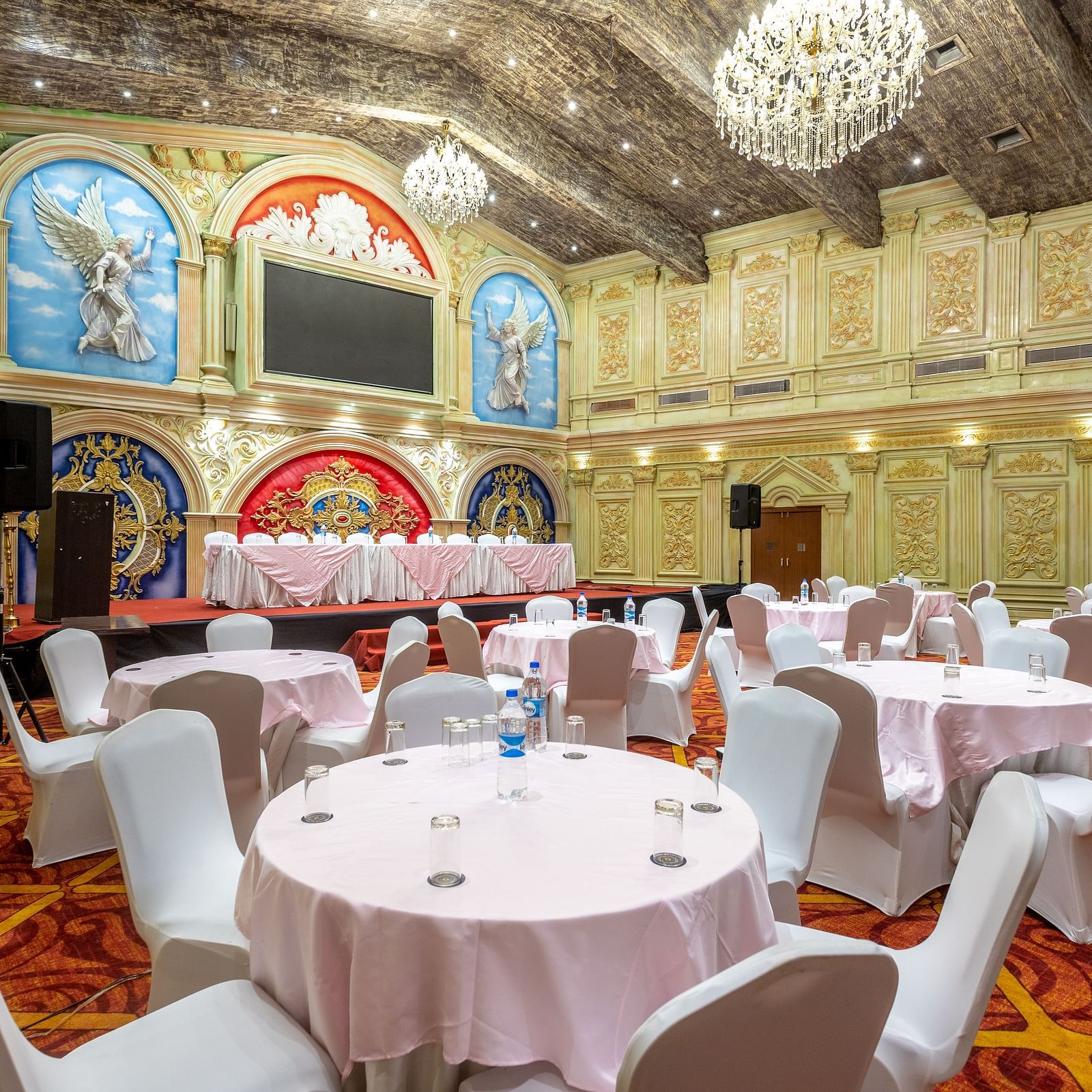 Ornate banquet hall at Diamond Palace Lords Plaza with round tables, chairs, chandeliers, and decorative walls.