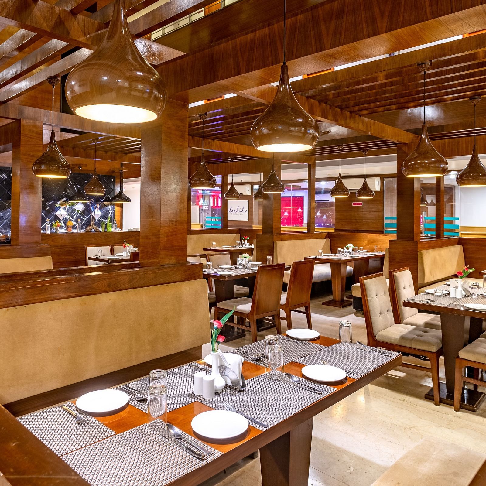 Warmly lit restaurant at Diamond Palace Lords Plaza with wooden beams, set tables, and booth seating.