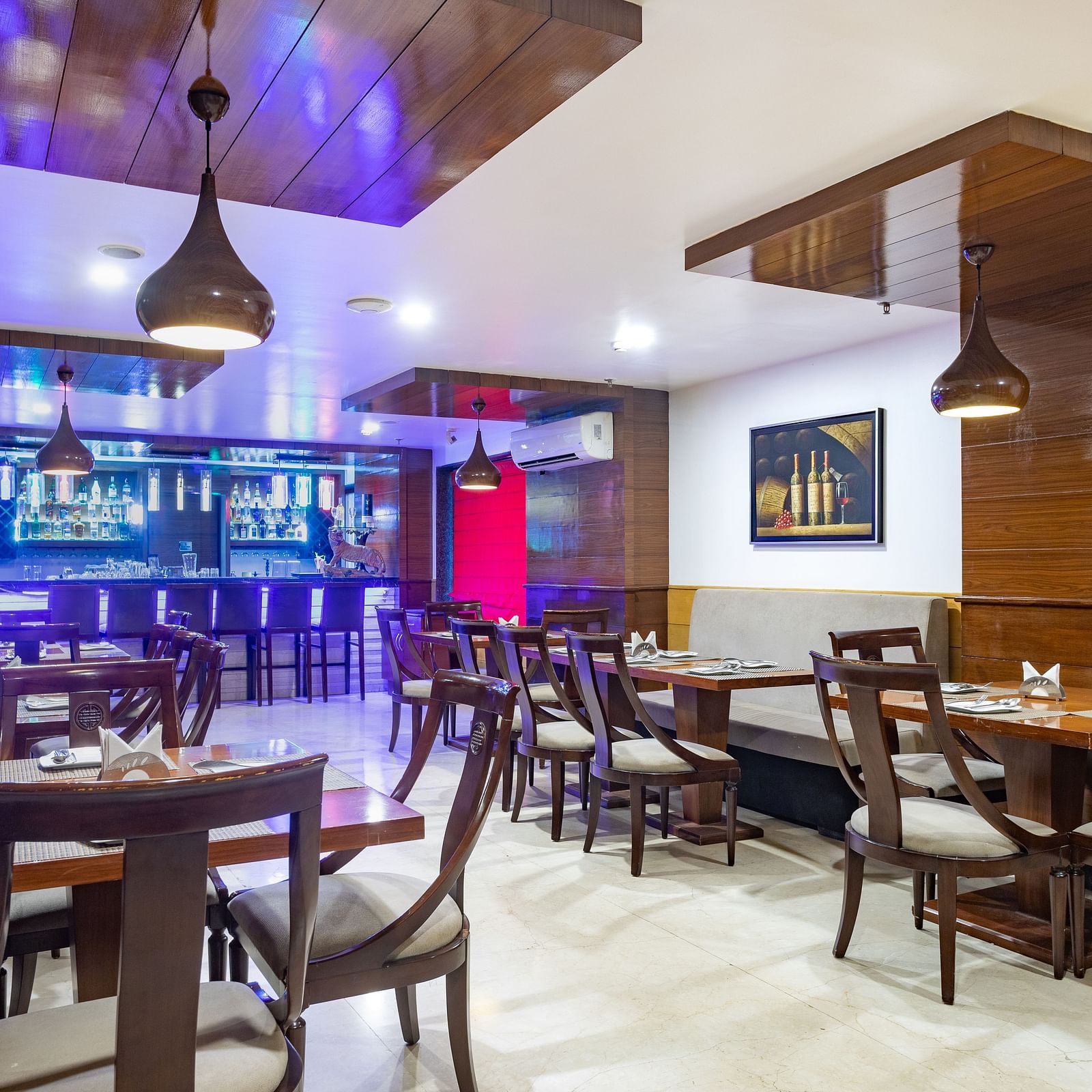 Modern restaurant at Diamond Palace Lords Plaza with wooden tables, chairs, pendant lights, and a bar area.