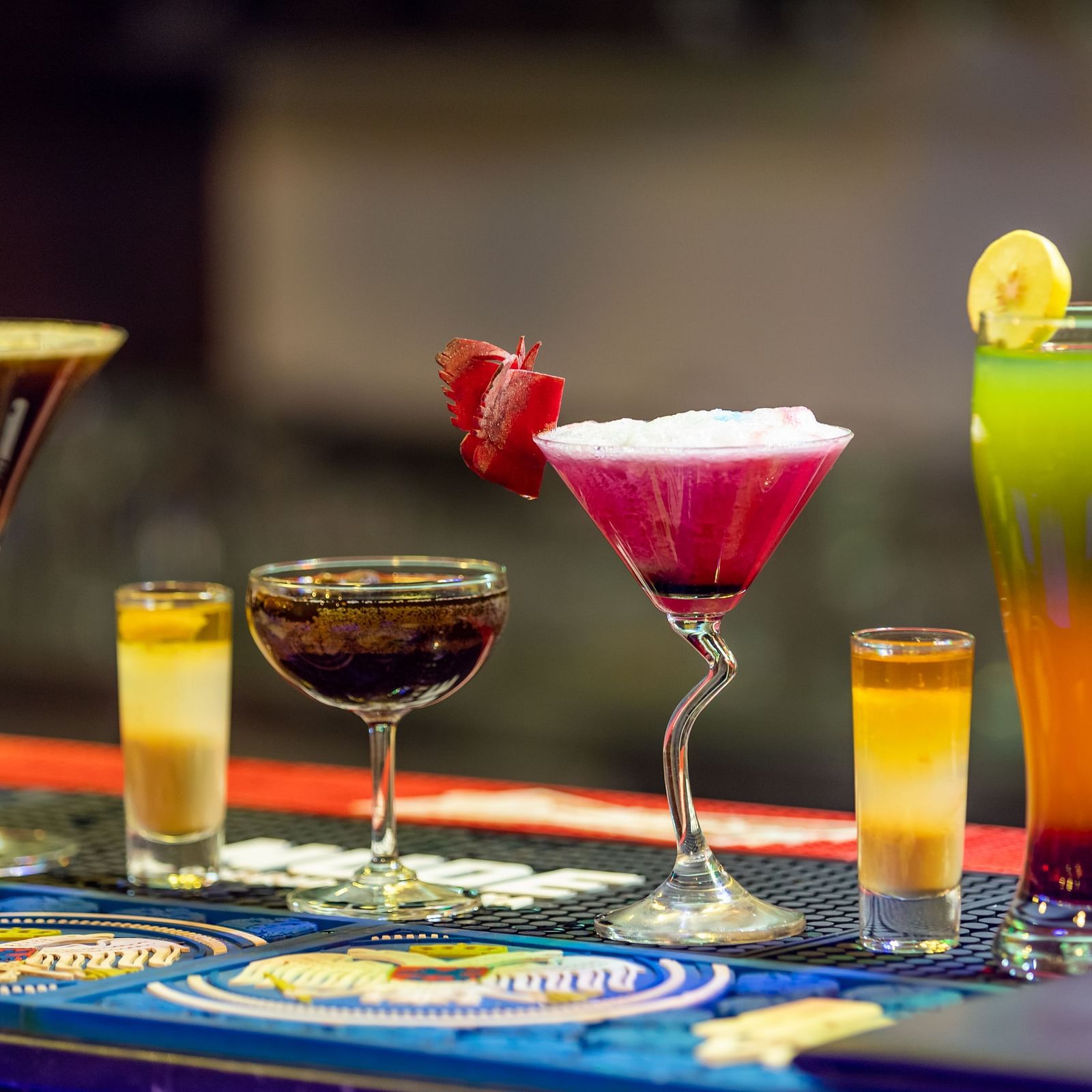 Assortment of colorful cocktails and shot glasses arranged on a bar counter with a blurred background.
