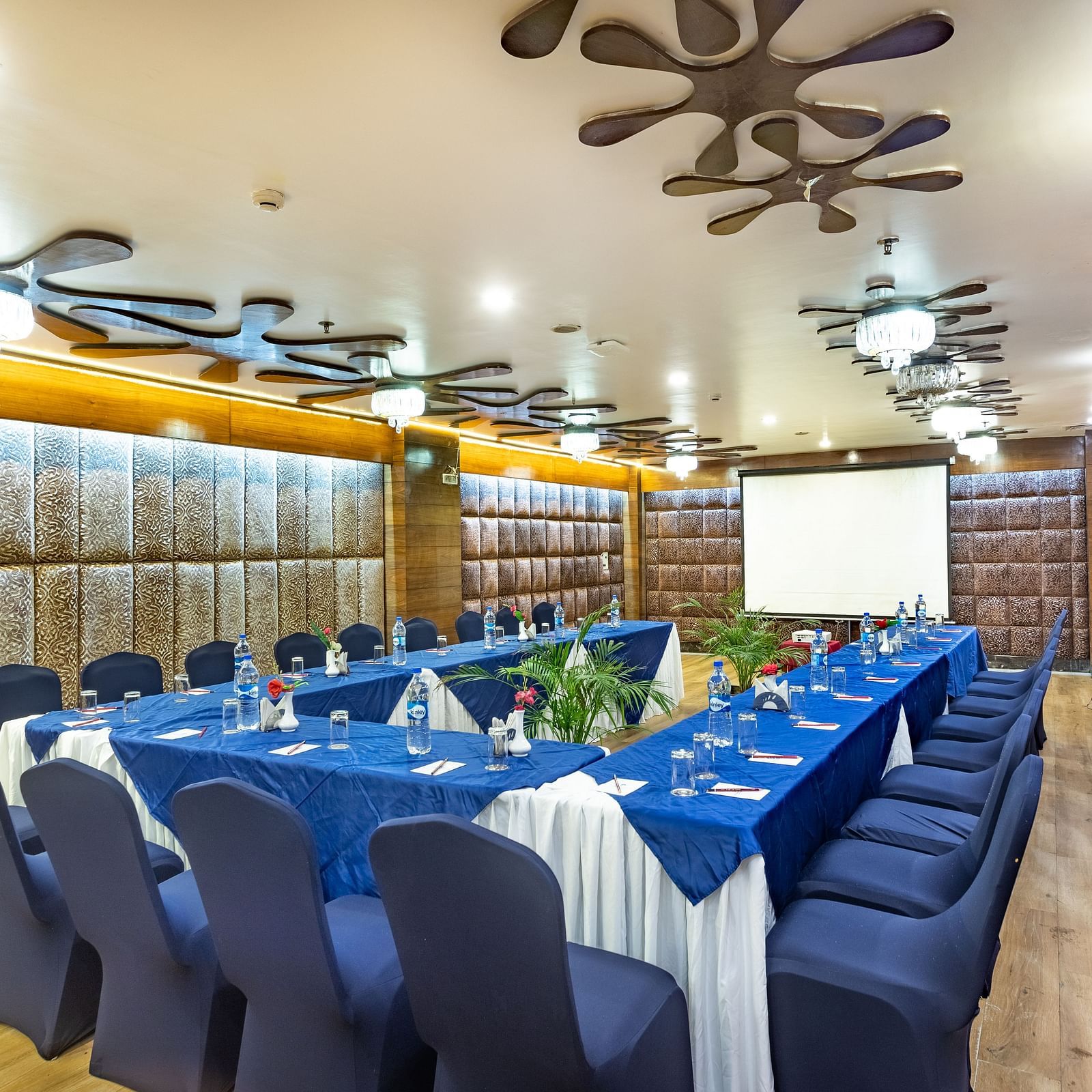 Meeting room with a U-shaped table covered in fabric, facing a projection screen and decorated walls.