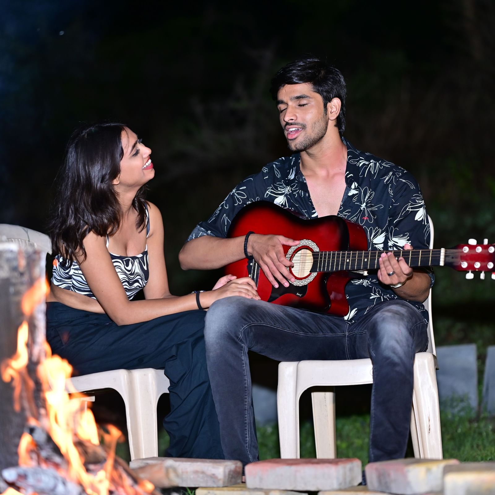 Couple playing guitar by a campfire at a camping site | Diamond Parks, Pune