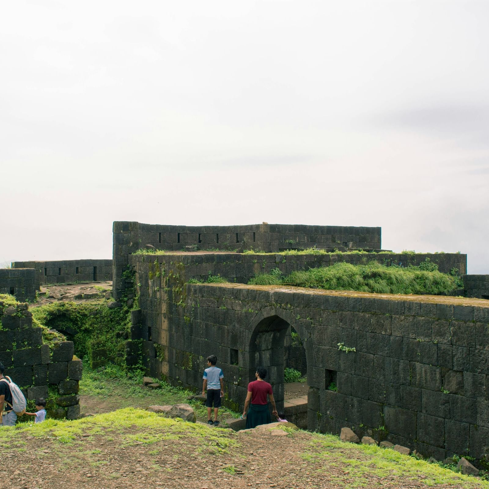 The entrance and stone walls of a historic fort, with a few people walking in the distance.