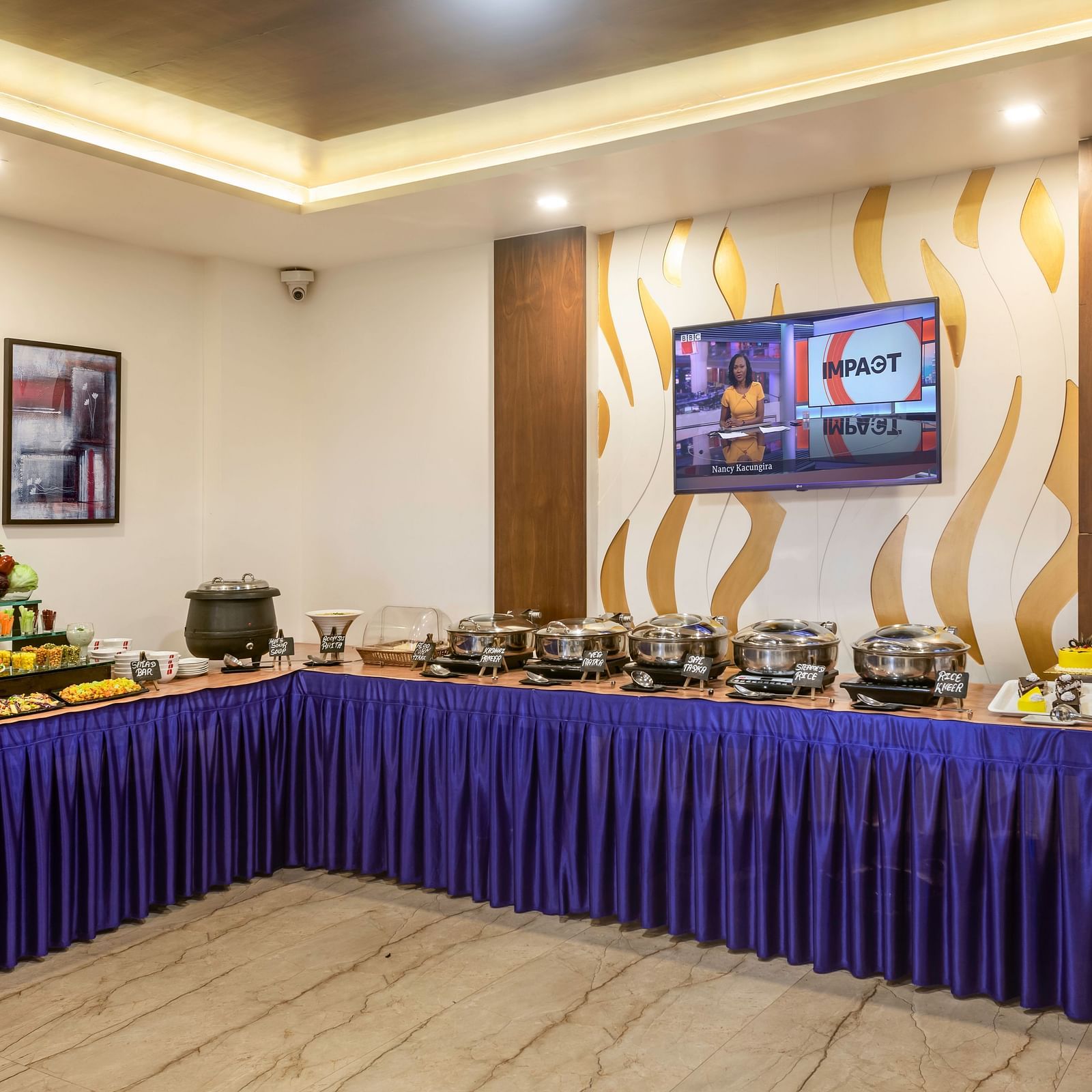 A buffet spread with various food items arranged on long tables draped with blue cloth in a well-lit room.
