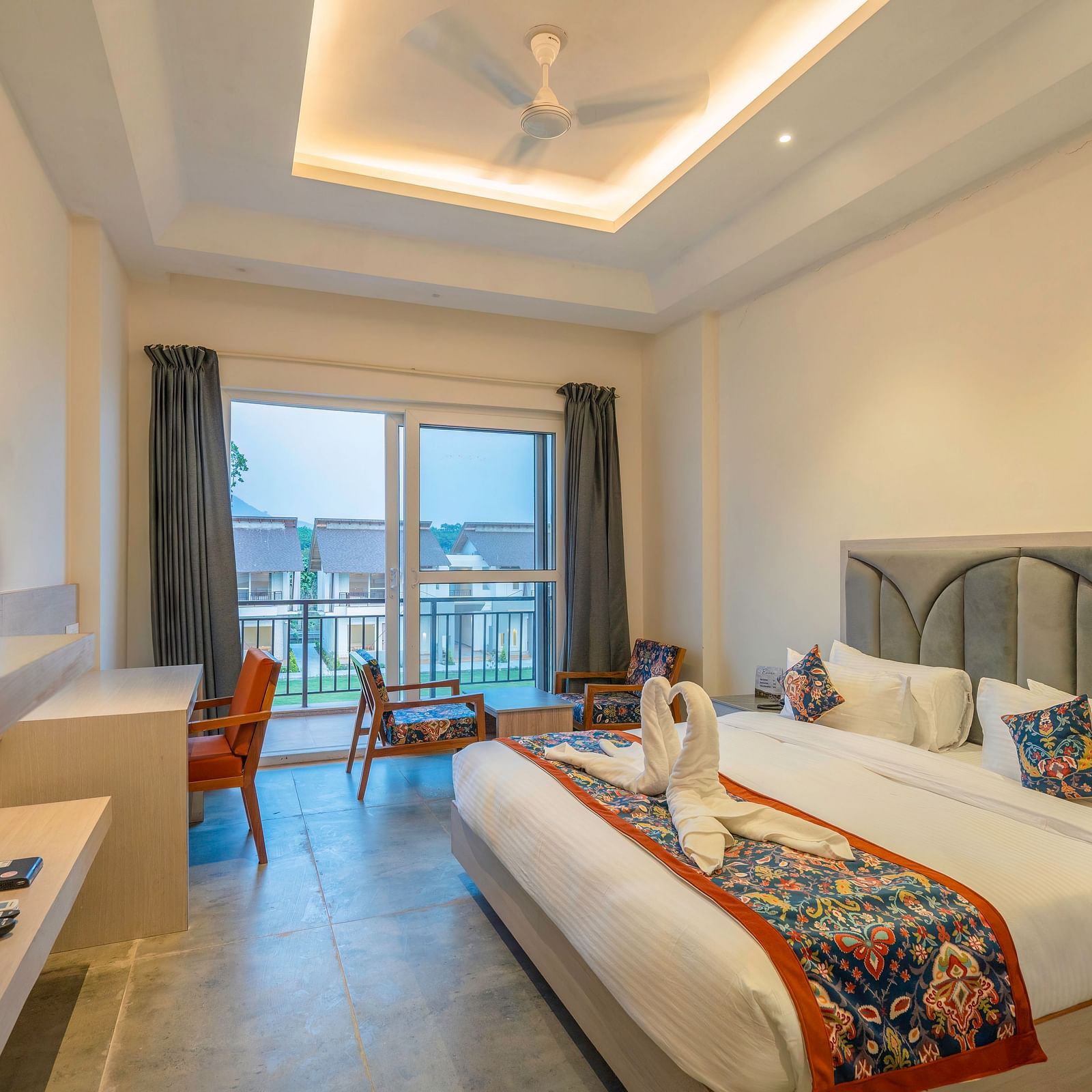 A modern hotel room with a king size bed, a flat-screen TV, and a balcony overlooking a scenic view.