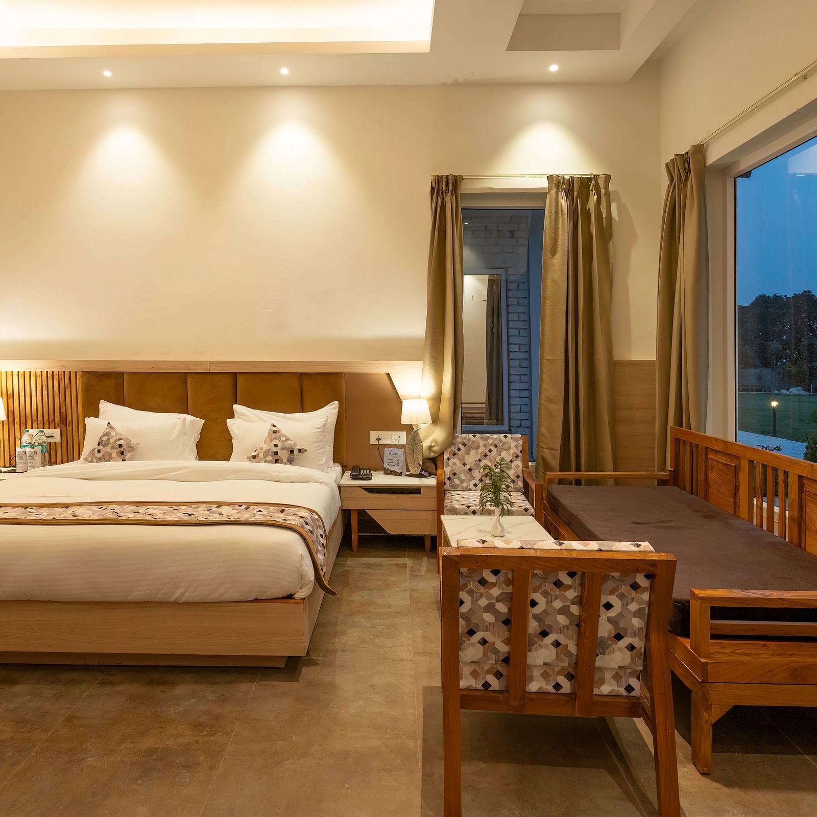 A cosy hotel room with a king-size bed, a seating area, and a view of the lush green outdoors.