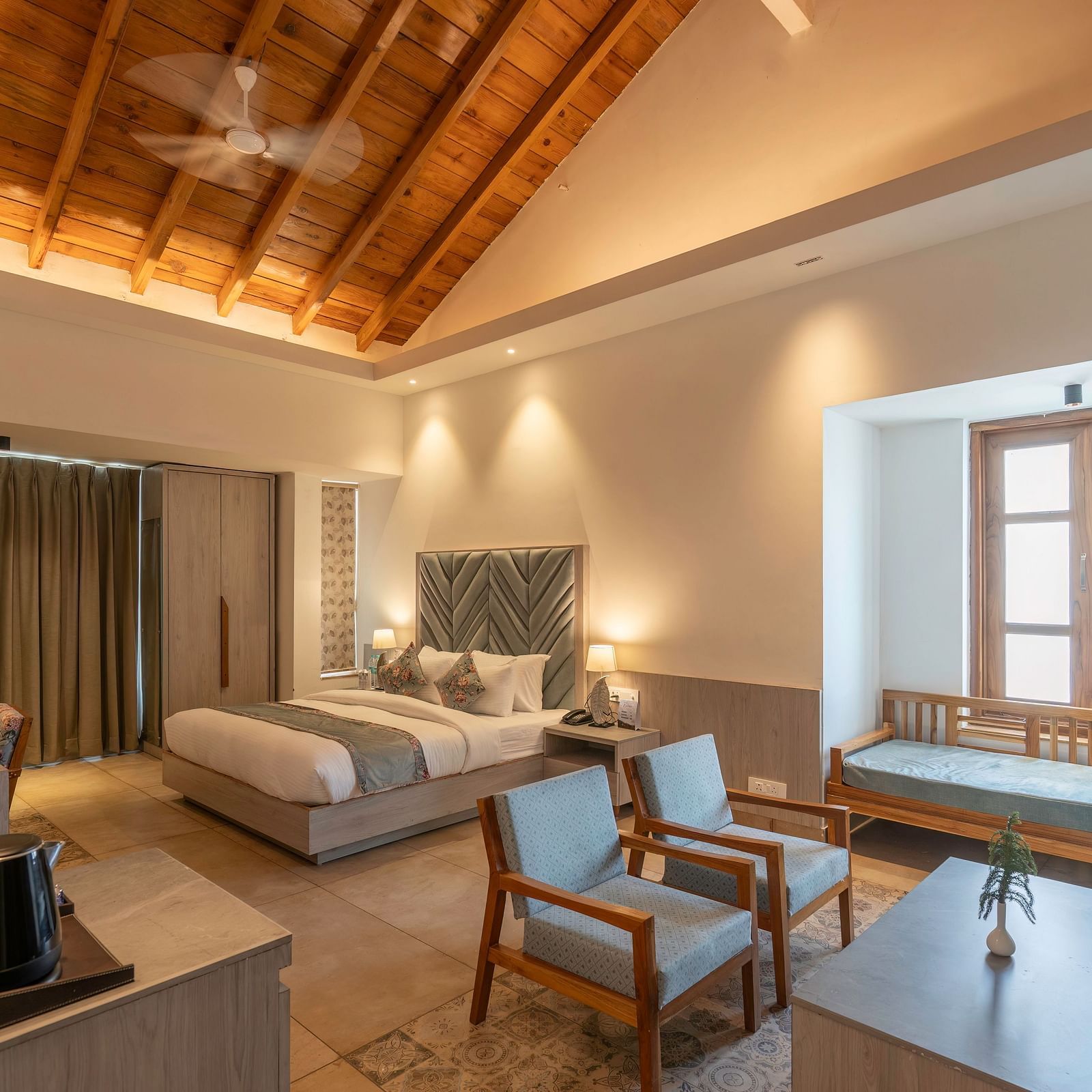 A spacious hotel room with a king size bed, a seating area, and a view of the lush green outdoors.