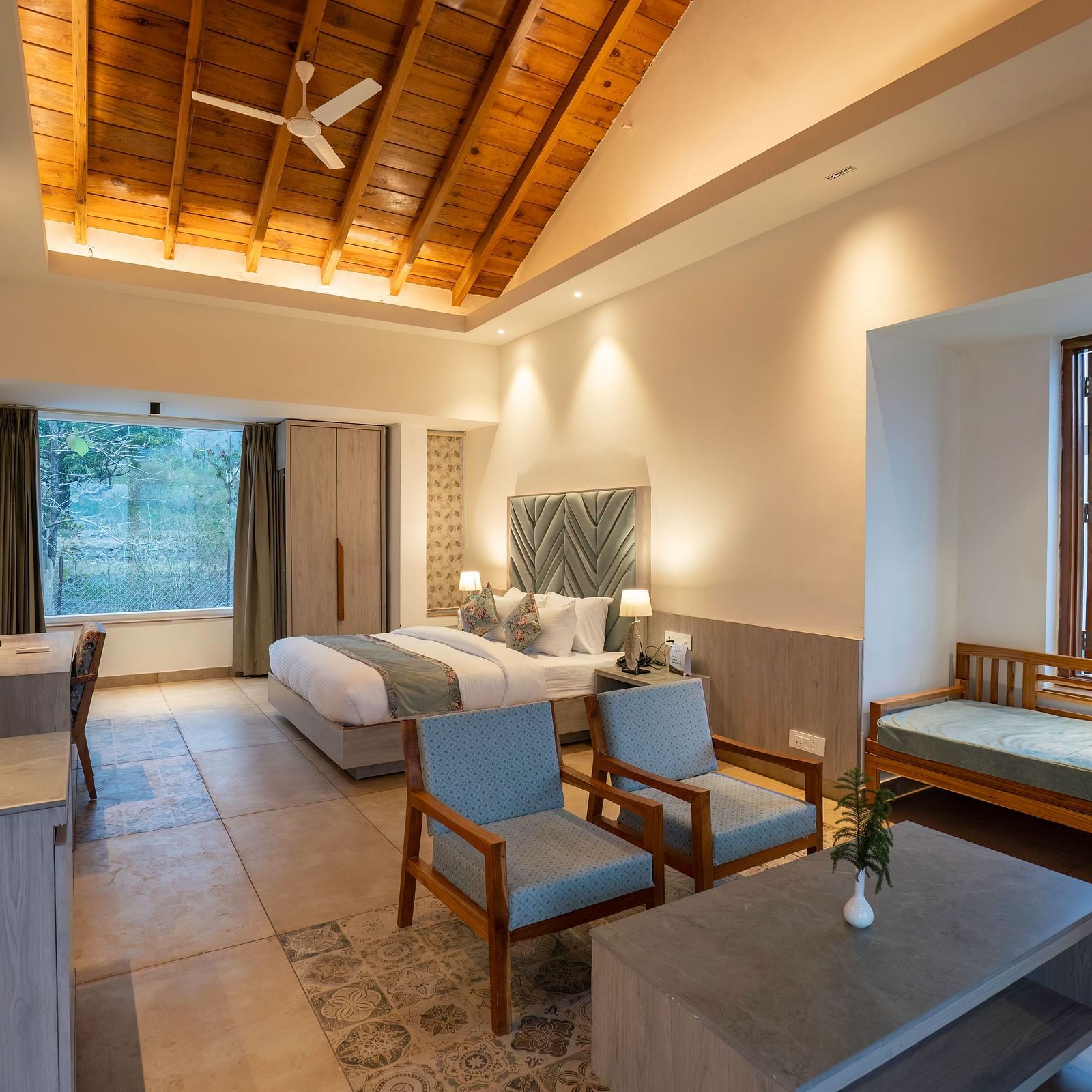 A spacious room with a king size bed, a seating area, and a view of the lush green outdoors.