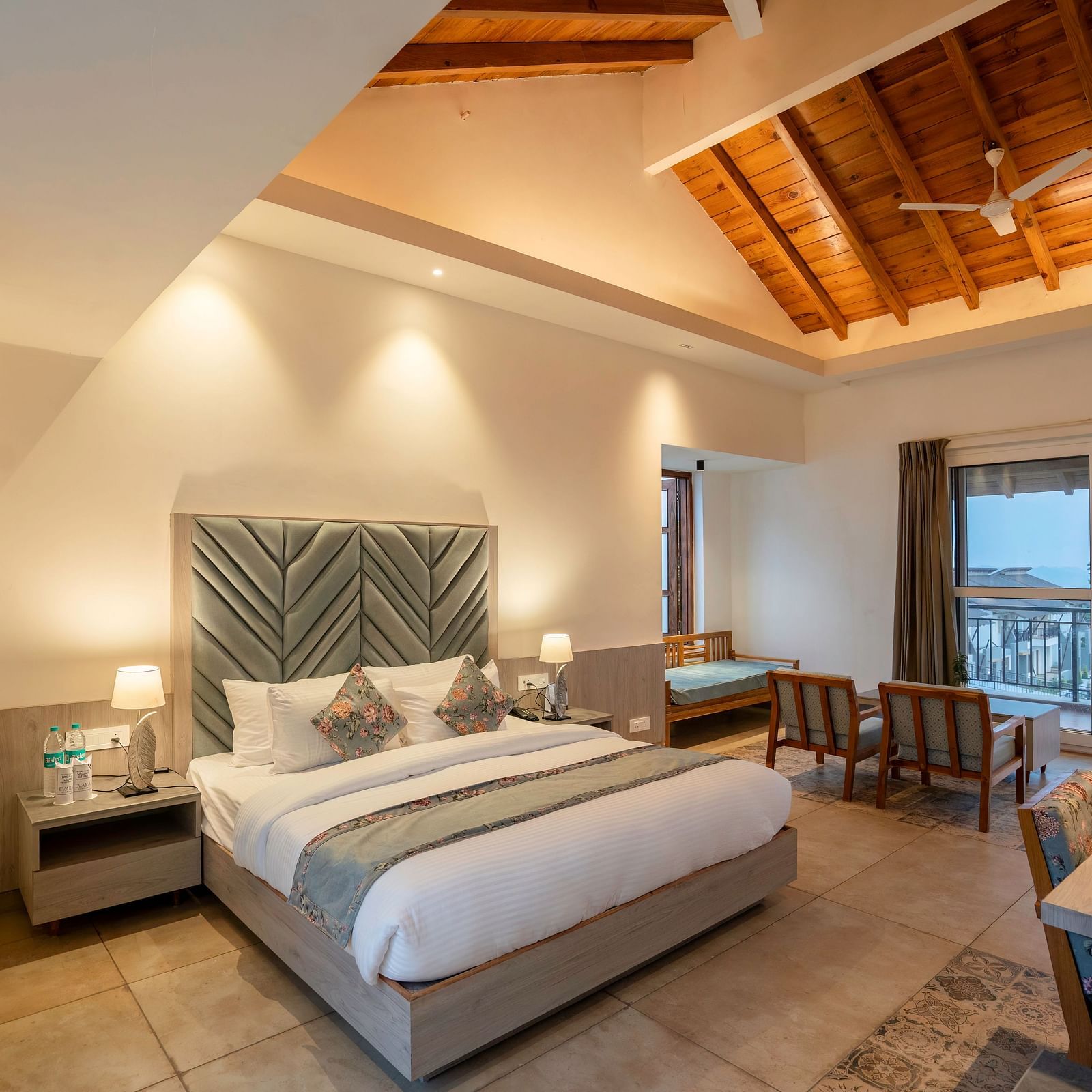 A modern hotel room with a king size bed, a seating area, and a view of the lush green outdoors.