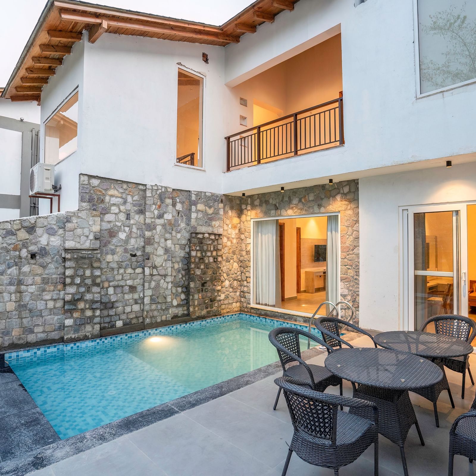 A shot of a vlla with a swimming pool and a patio, surrounded by lush greenery.
