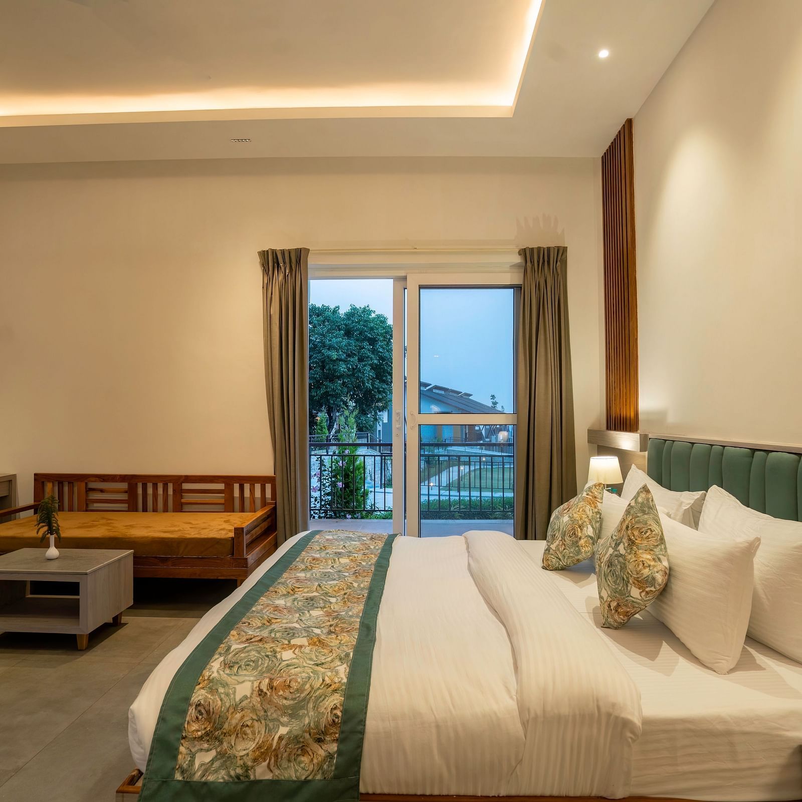 A modern hotel room with a king-size bed, a seating area, and a balcony offering a view of the lush green mountains.