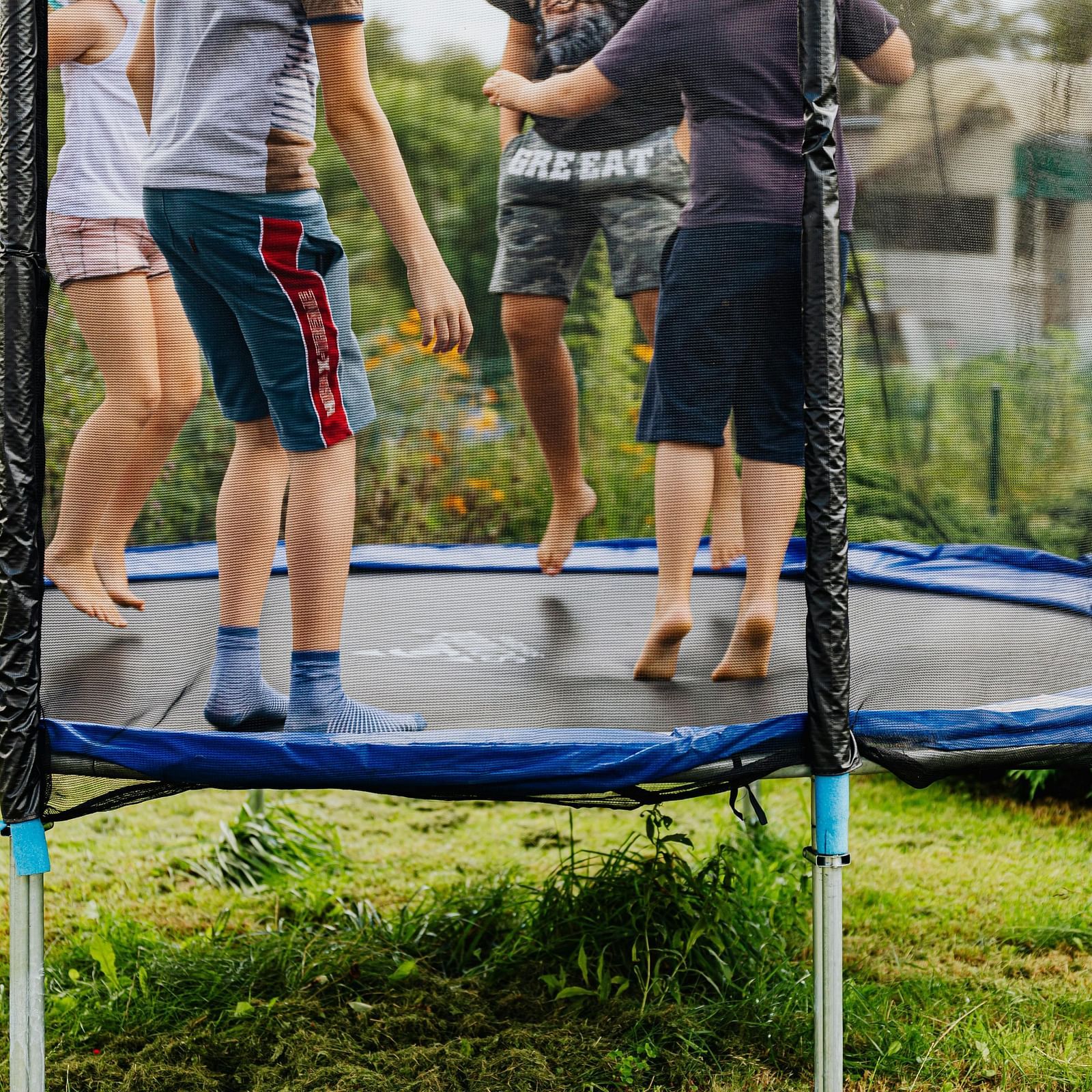 This image shows a trampoline with a blue mat and a safety net. The trampoline is set up outdoors, with a clear blue sky visible in the background.