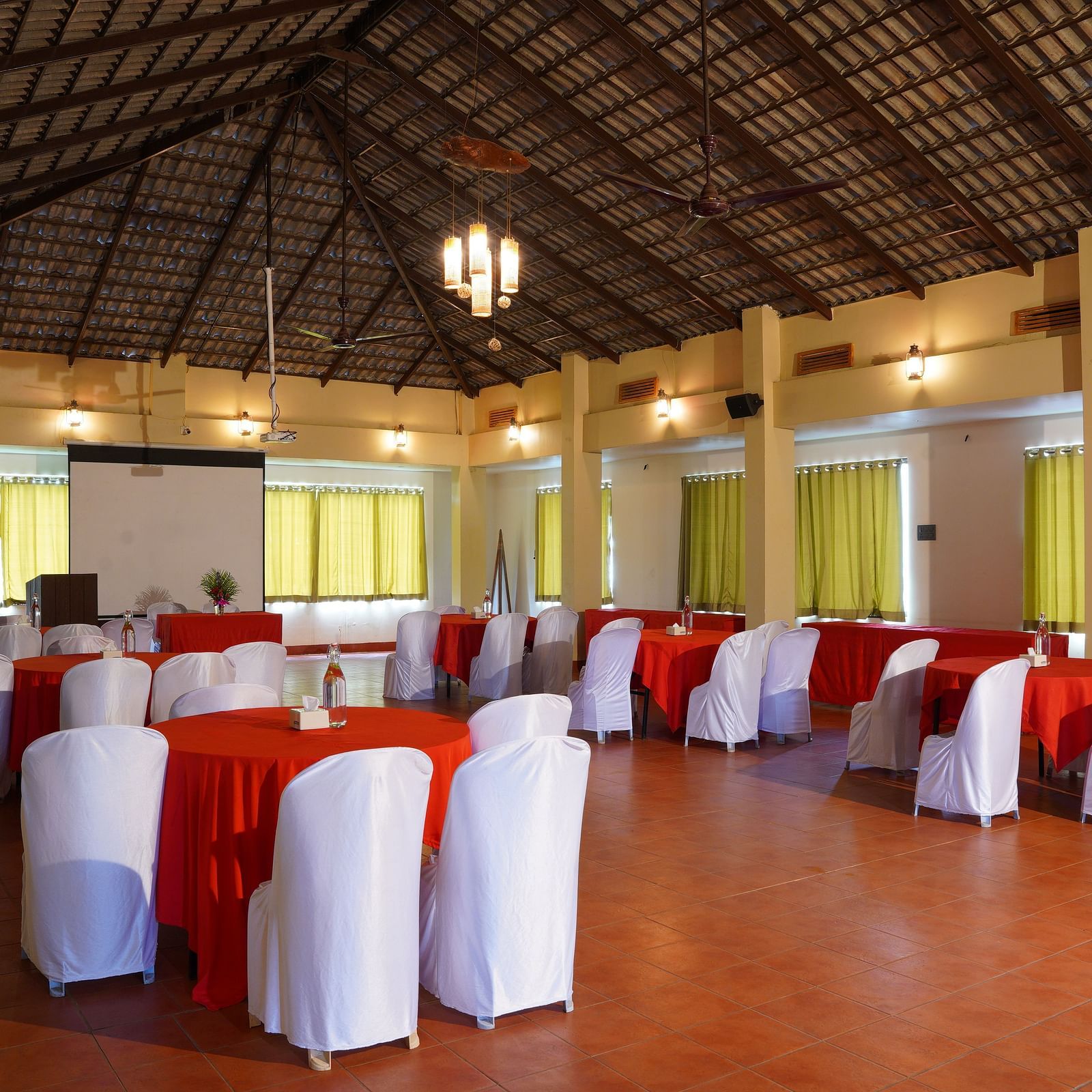 Another view of the banquet hall at Forest Escapes Koyna, showing rows of tables with red accents and white chairs.