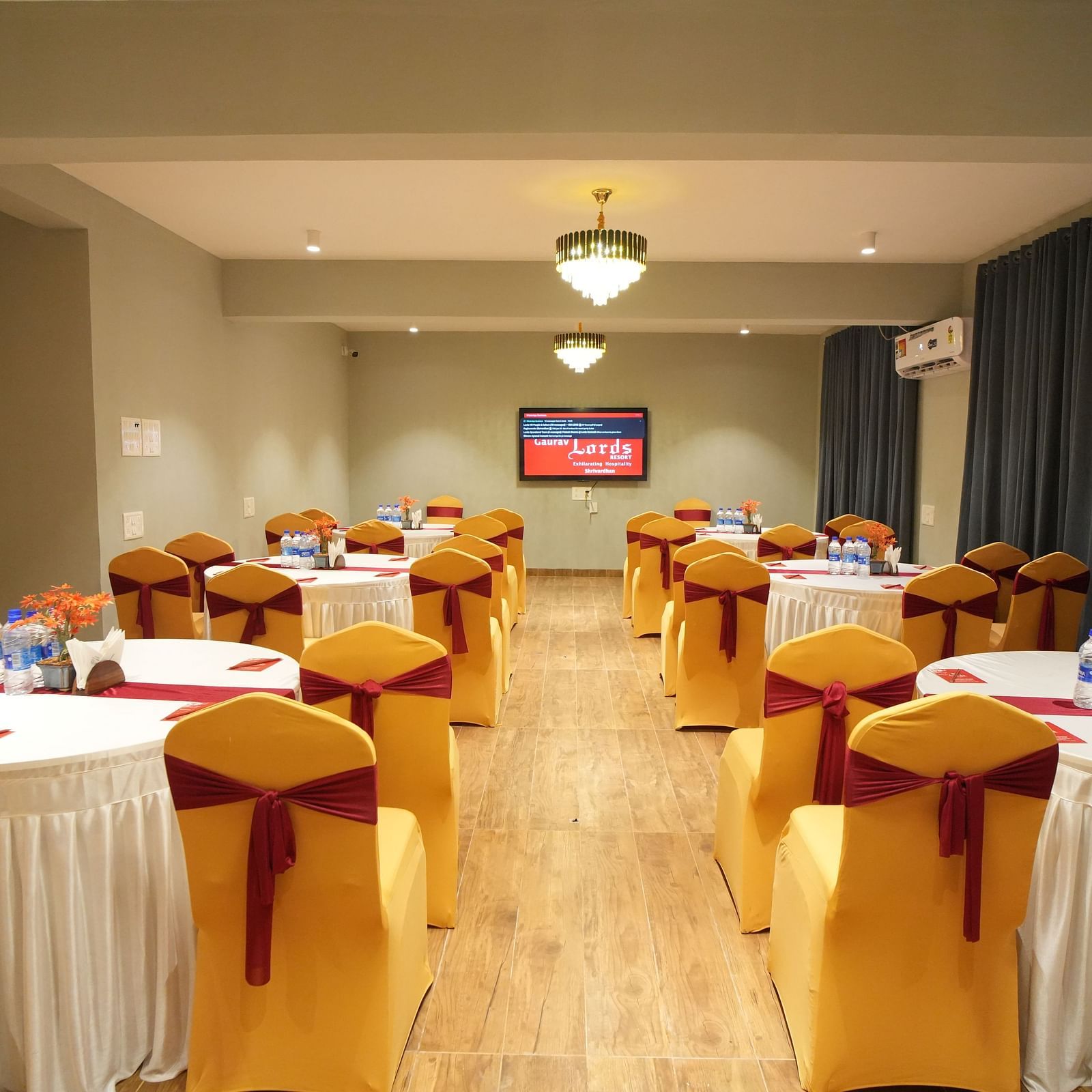 A class room style seating area with tables and chairs, TV and chandelier lighting 