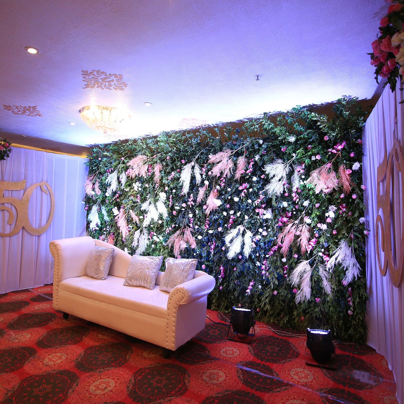 A stage at a banquet hall featuring a green and white floral wall, a white couch, and red carpet at Hotel Ashok Nagpur.