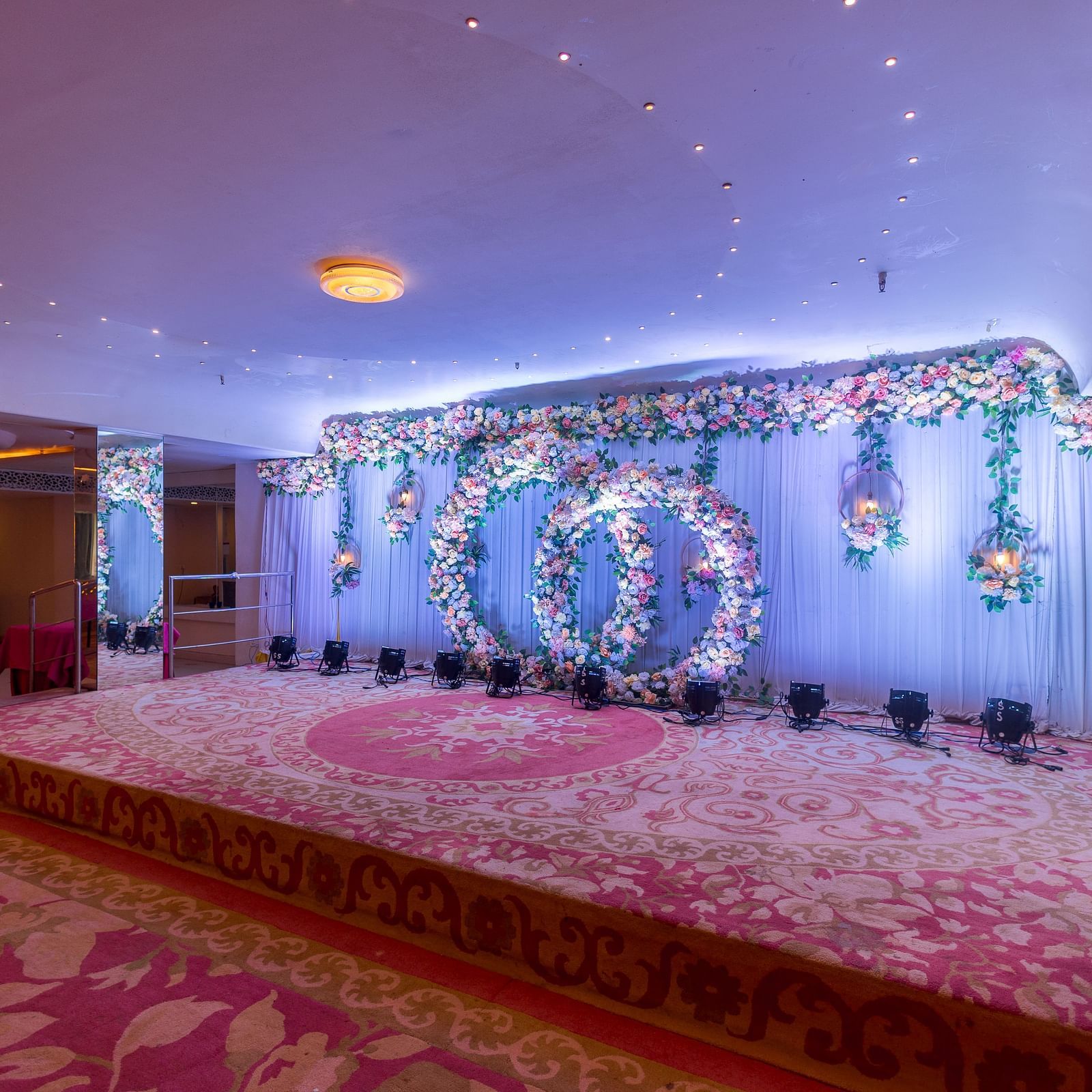 A decorated stage with floral arrangements and lighting, likely set up for an event at Hotel Ashok Nagpur.