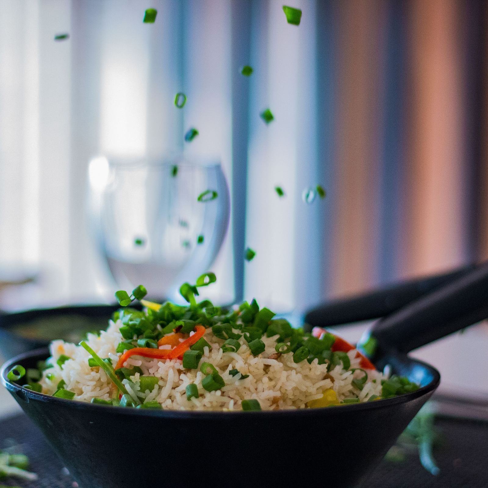 A black bowl filled with rice and green peas, with more peas being sprinkled from above.