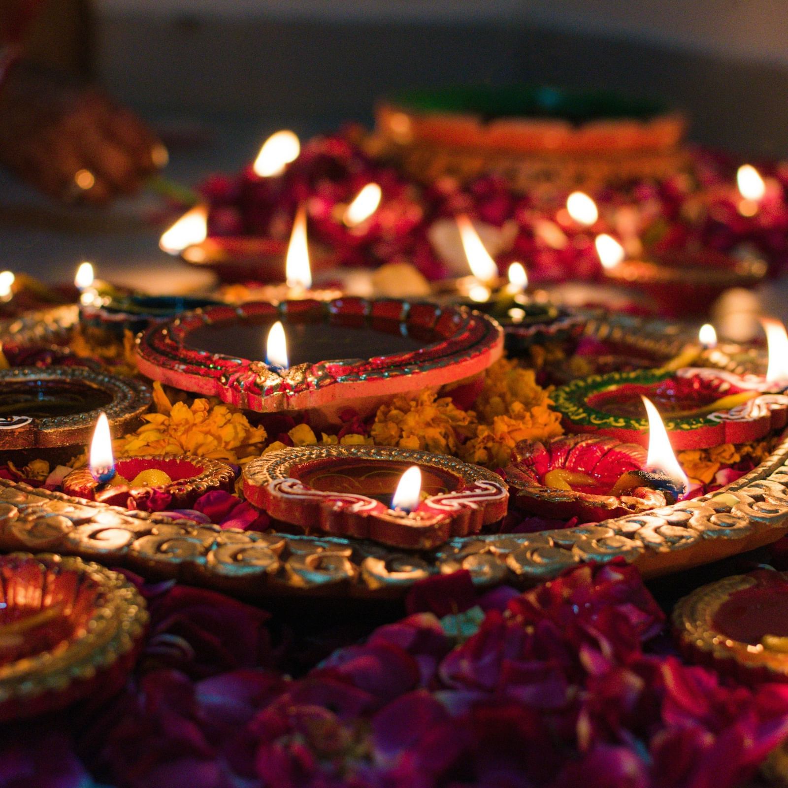 Small oil lamps lit during a hindu festival and the lamps are surrounded with flowers and loose petals.