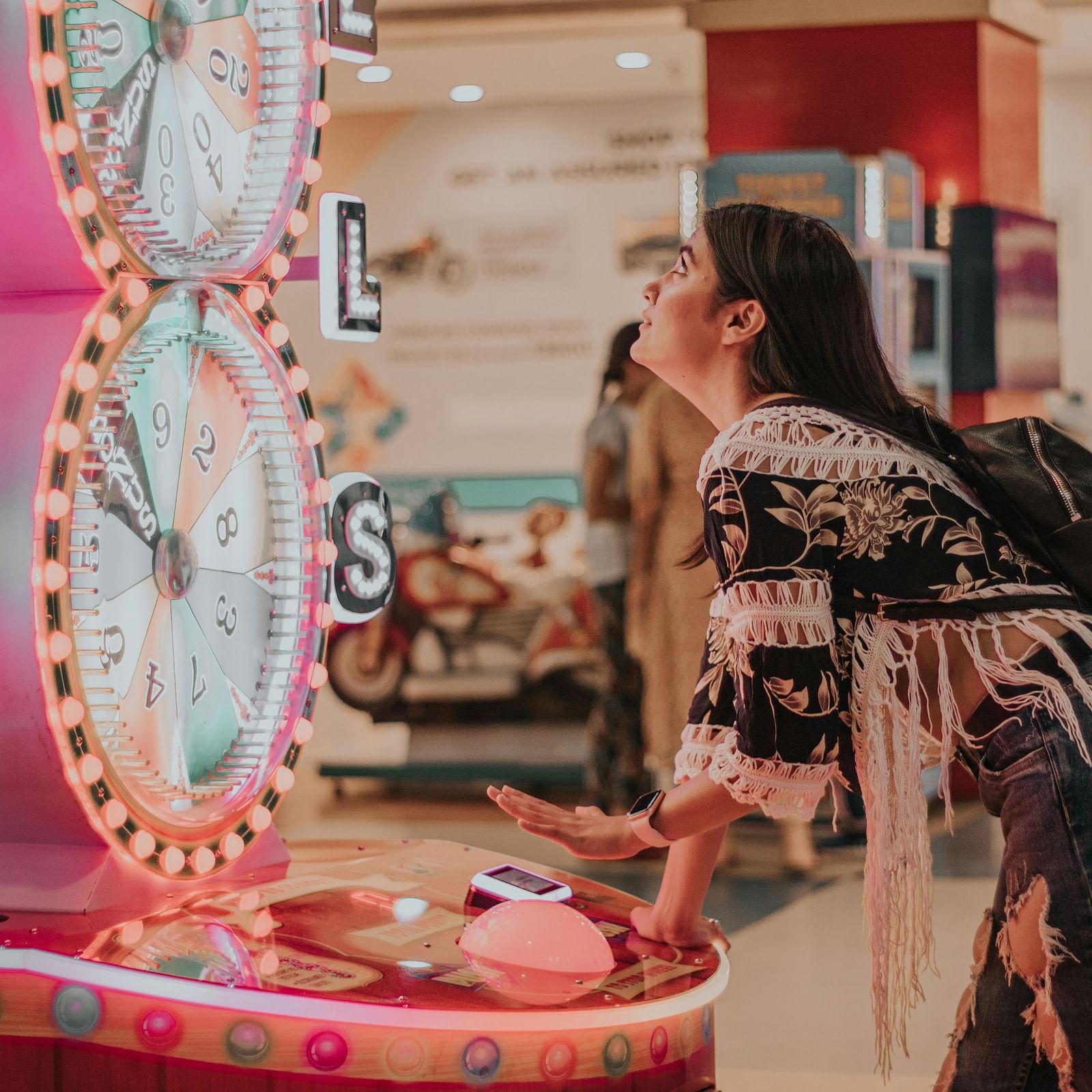 A young woman enjoying an arcade game in a shopping centre, with bright decor and neon signage.