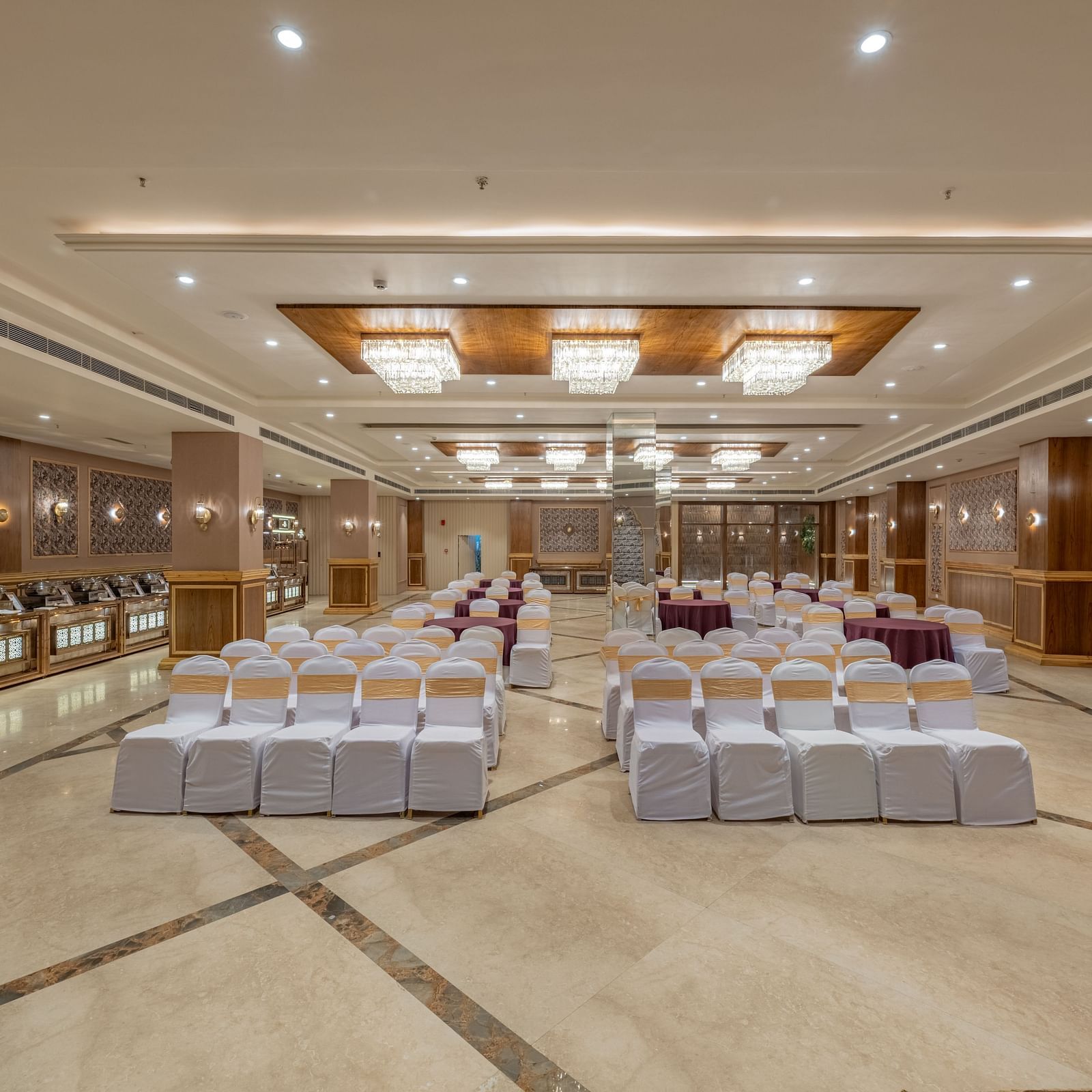 Large banquet hall at Hotel Highway King, Bagru, with rows of chairs, decorative ceiling lights, and mirrored wall panels.