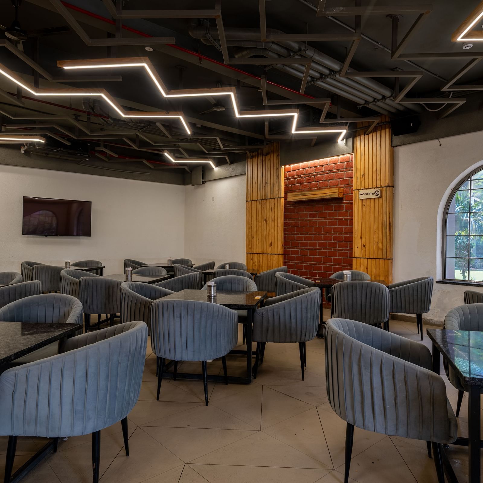 Indoor dining area at Hotel Highway King, Bagru, with multiple tables, upholstered chairs, and modern ceiling lighting.