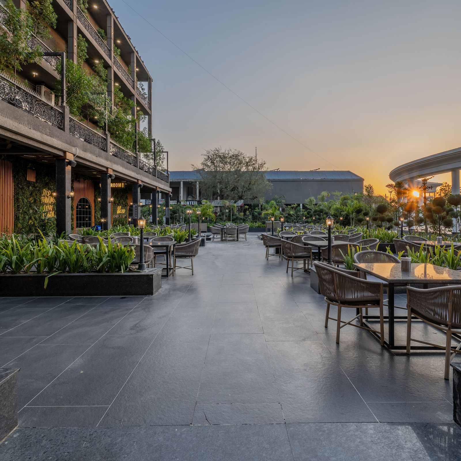 Outdoor seating area at Hotel Highway King, Bagru, with tables, chairs, greenery, and the hotel building in the background.