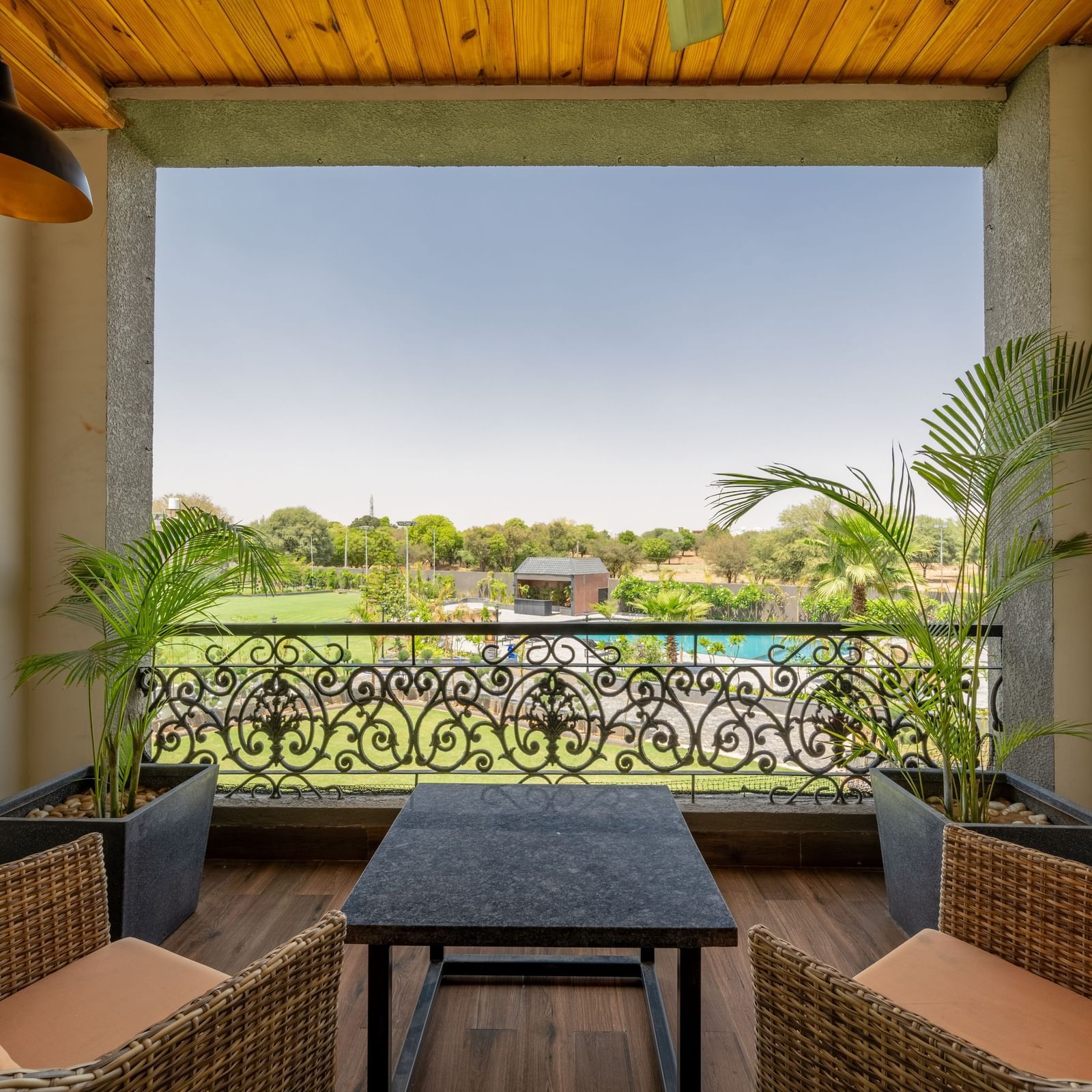 A balcony of executive king room in Hotel Highway King, Bagru, featuring cushioned lounge chairs and a coffee table, overlooking lush garden under an overcast sky.